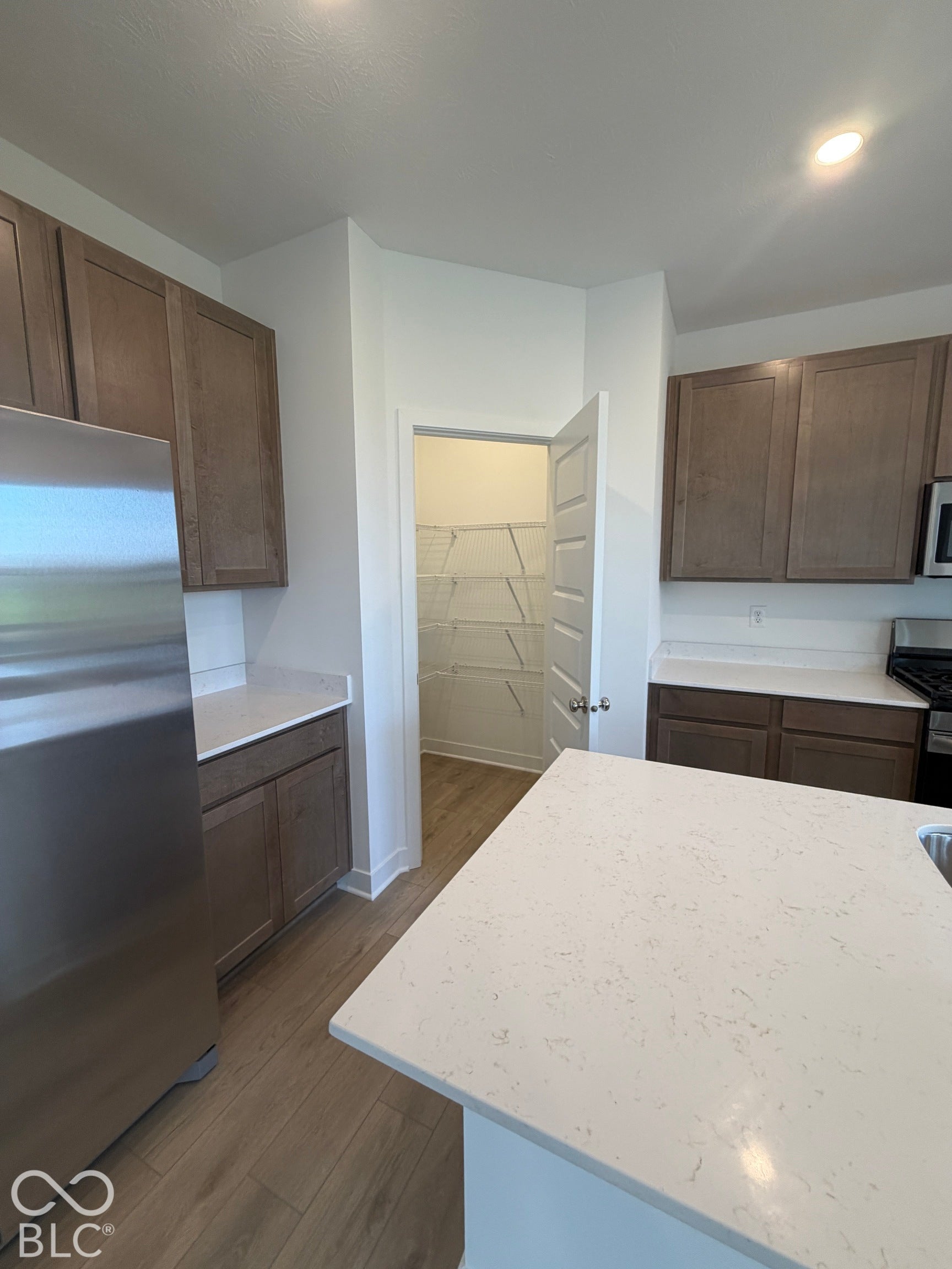 Kitchen featuring stained wood cabinetry, stone-finish countertops, stainless steel appliances, and a walk-in pantry with wire shelving