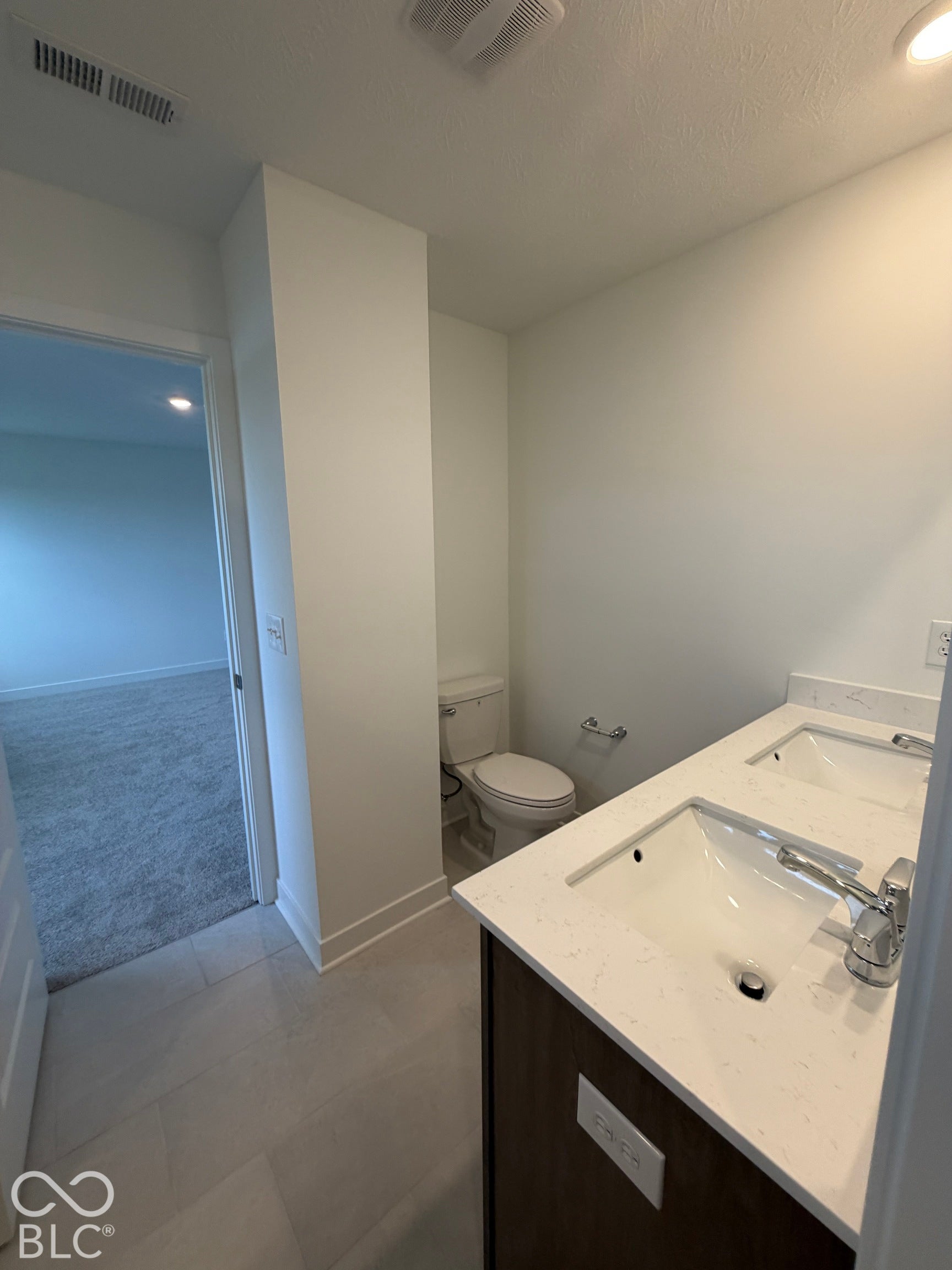 Double vanity with a white countertop and undermount sinks, featuring dark-finish cabinetry, ceramic-tile flooring, and a standard-height toilet