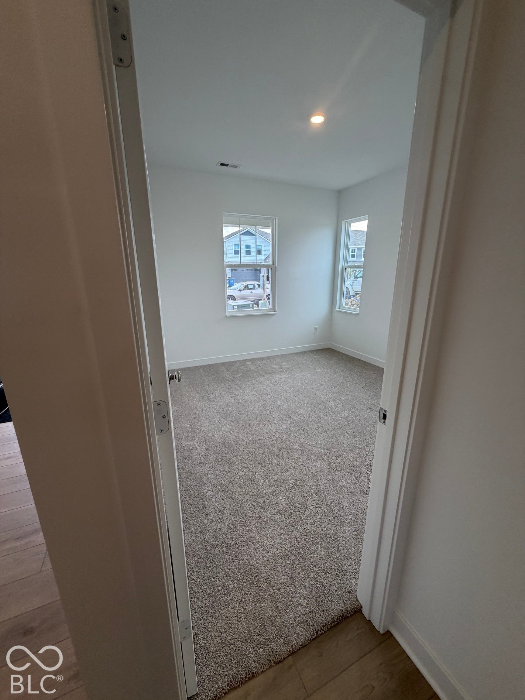 Neutral-toned wall-to-wall carpeting, two double-hung windows with exterior muntin detailing, and recessed ceiling lighting