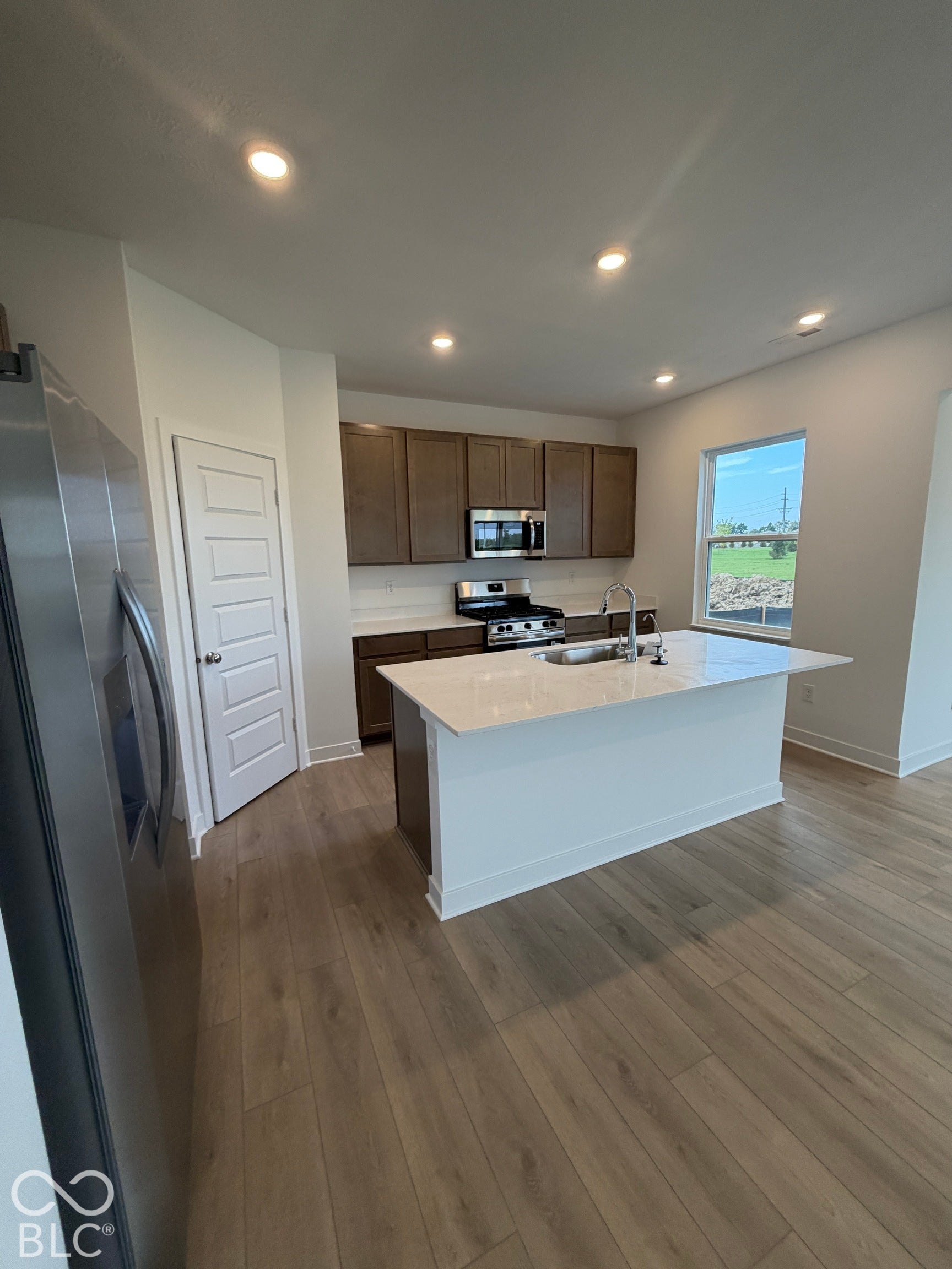 Kitchen featuring a central island with a solid surface countertop, wood-finish cabinetry, stainless steel appliances, and recessed lighting throughout
