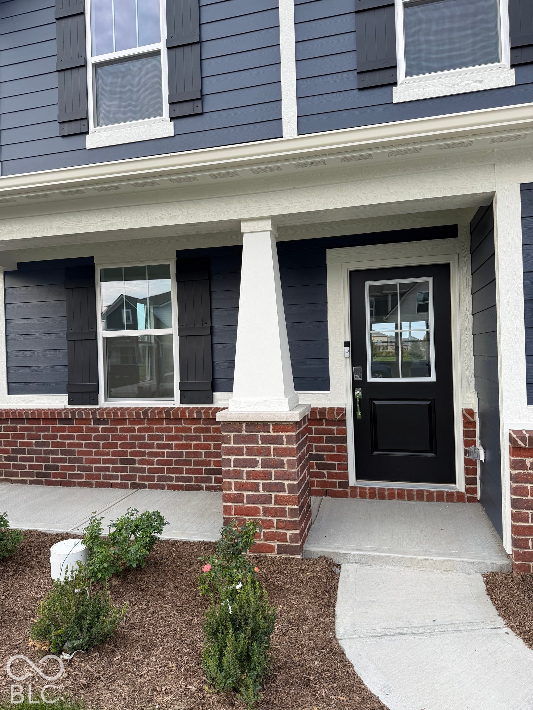 Exterior facade featuring dark horizontal siding, red brick masonry base, decorative shutters, and a covered entry with a tapered column