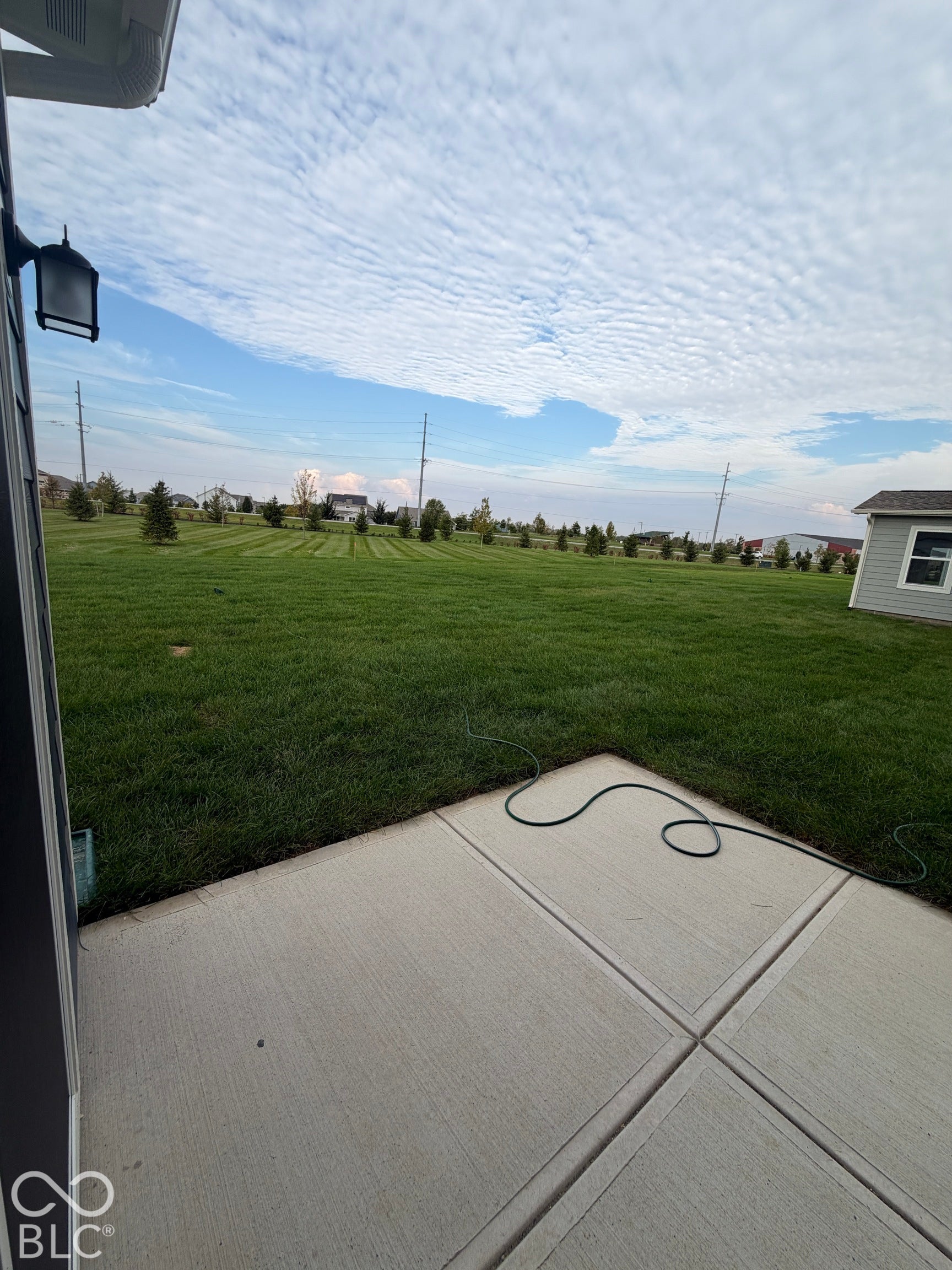 Concrete patio featuring a large, expansive lawn and exterior wall-mounted lighting