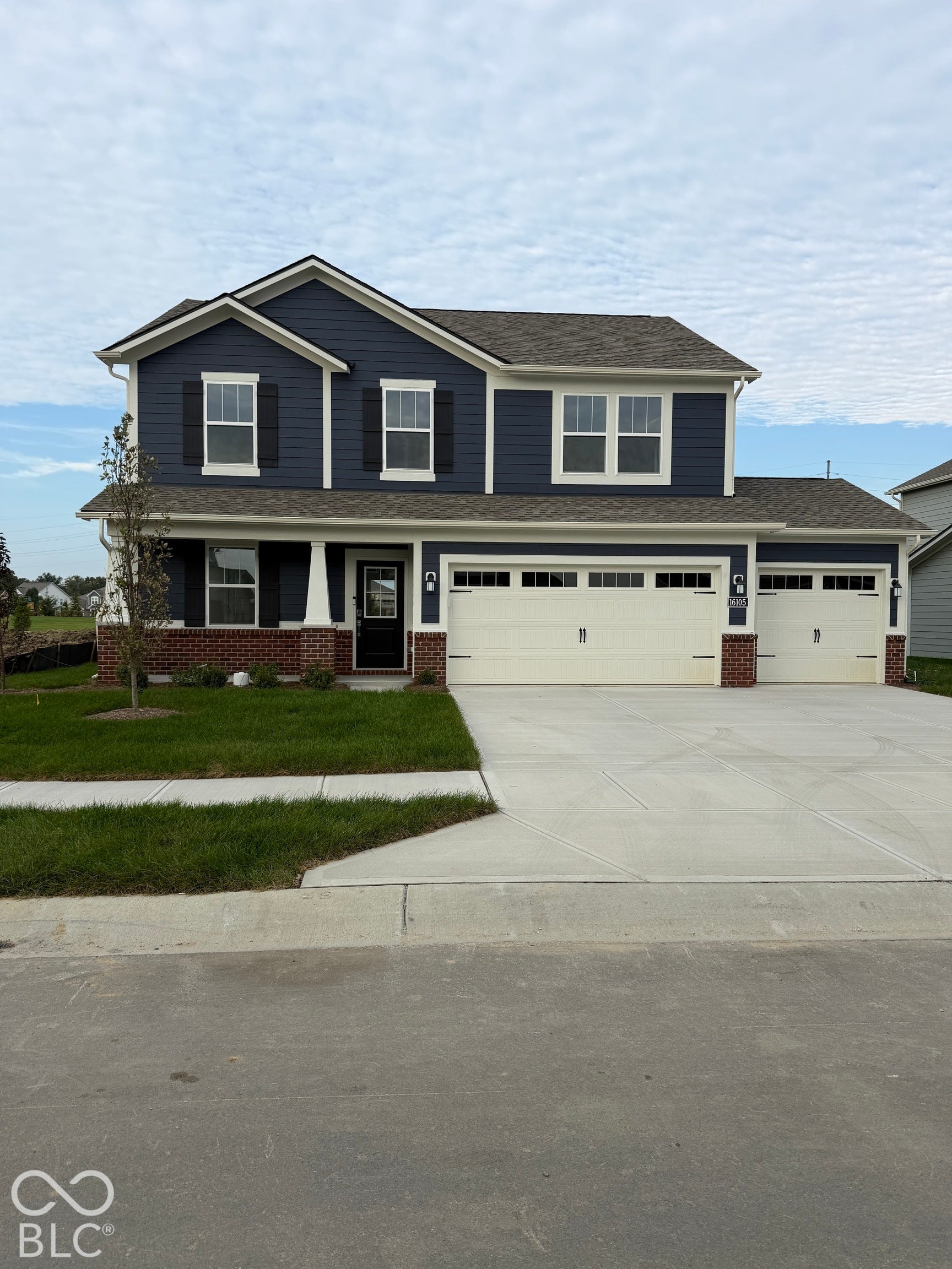 Two-story residence featuring blue horizontal siding, brick masonry detailing, a concrete driveway, a three-car garage, and shutter-accented windows