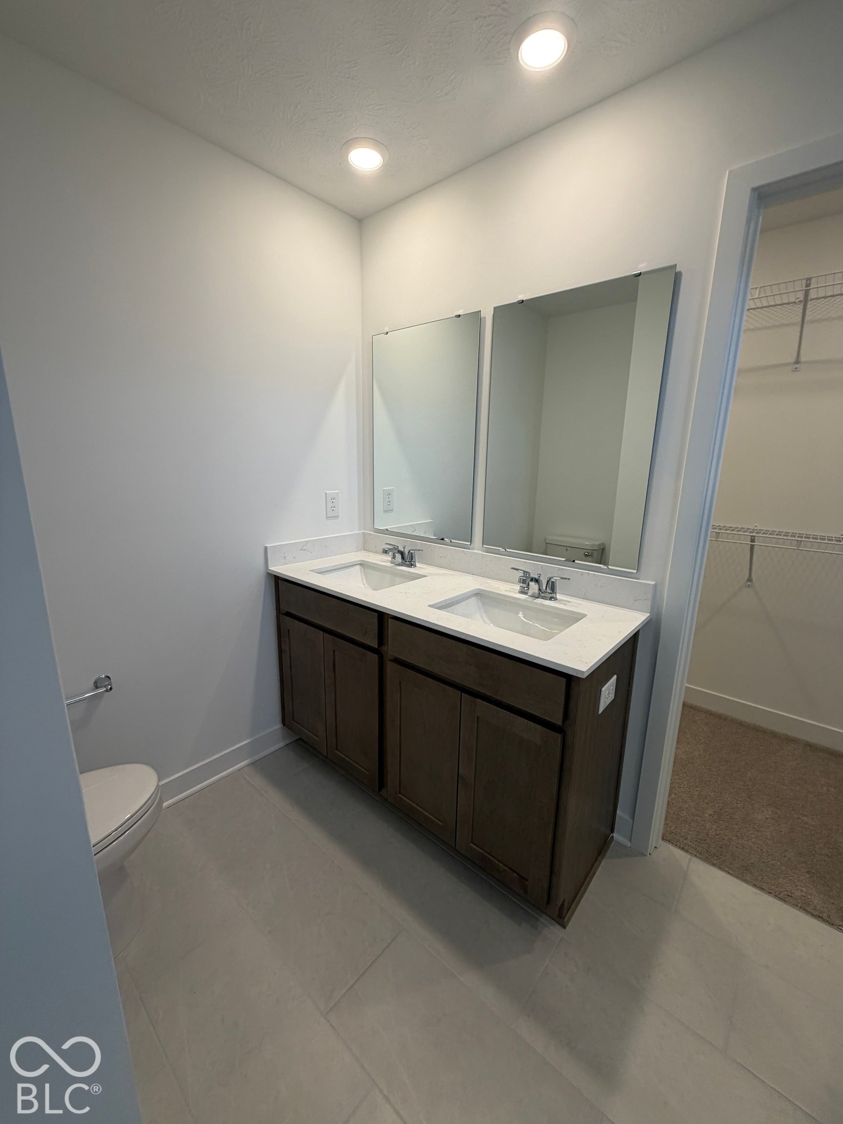 Dual-sink vanity with a solid-surface countertop, dark wood-finish cabinetry, rectangular under-mount sinks, and two wall-mounted mirrors