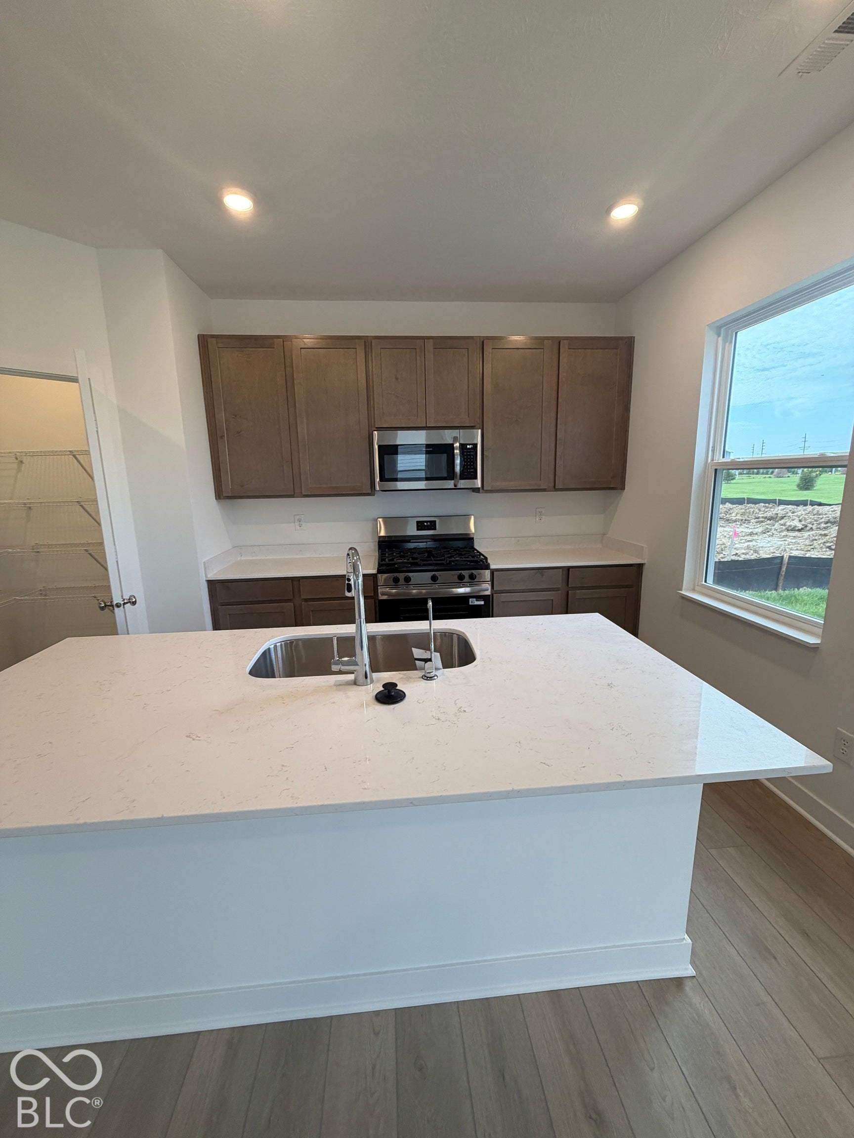 Kitchen featuring a center island with a stone-finish countertop and undermount sink, shaker-style cabinetry, stainless steel appliances, and wood-finish flooring