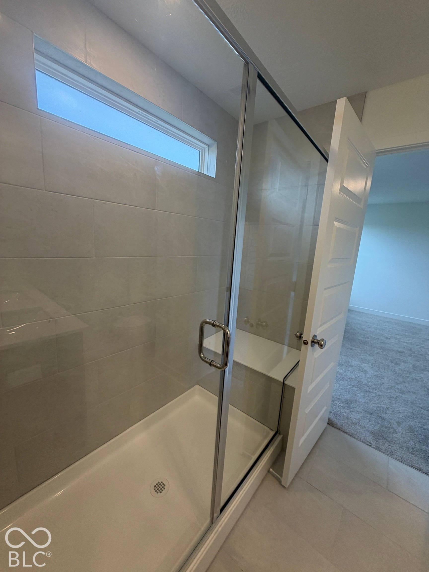 Walk-in shower featuring large-format wall tile, glass enclosure with brushed metal hardware, transom window, and built-in bench seat