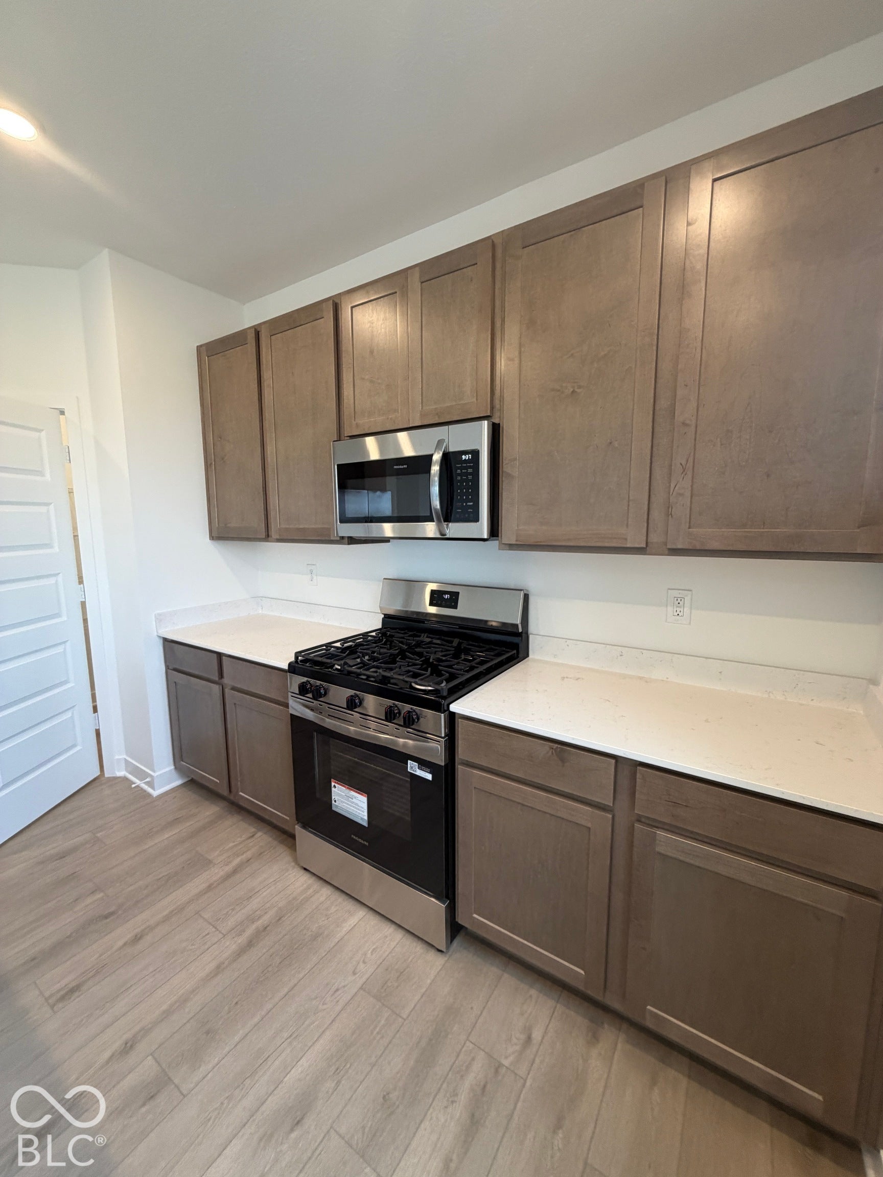 Kitchen featuring flat-panel wood-finish cabinetry, light-toned stone-composite countertops, stainless steel gas range, and wood-finish flooring