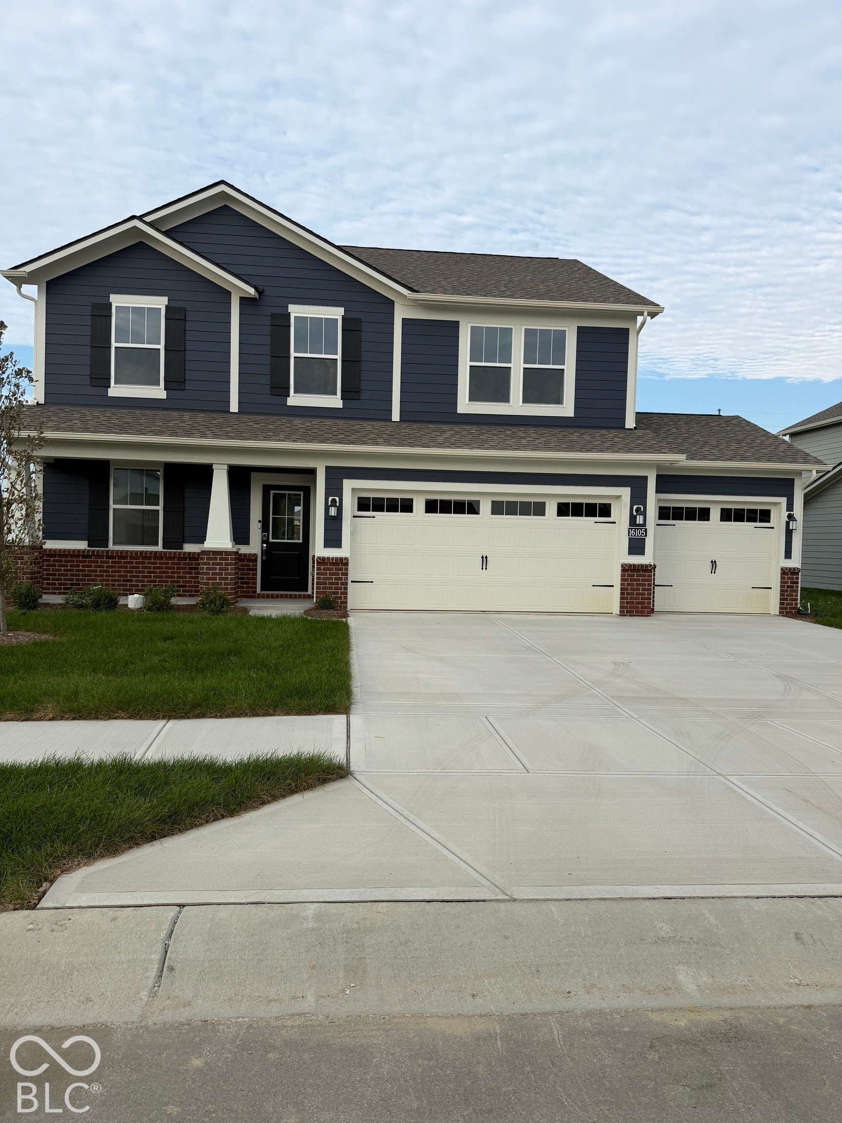 Two-story exterior featuring blue horizontal siding, red brick veneer accents, a covered front porch with a support column, and a three-car garage