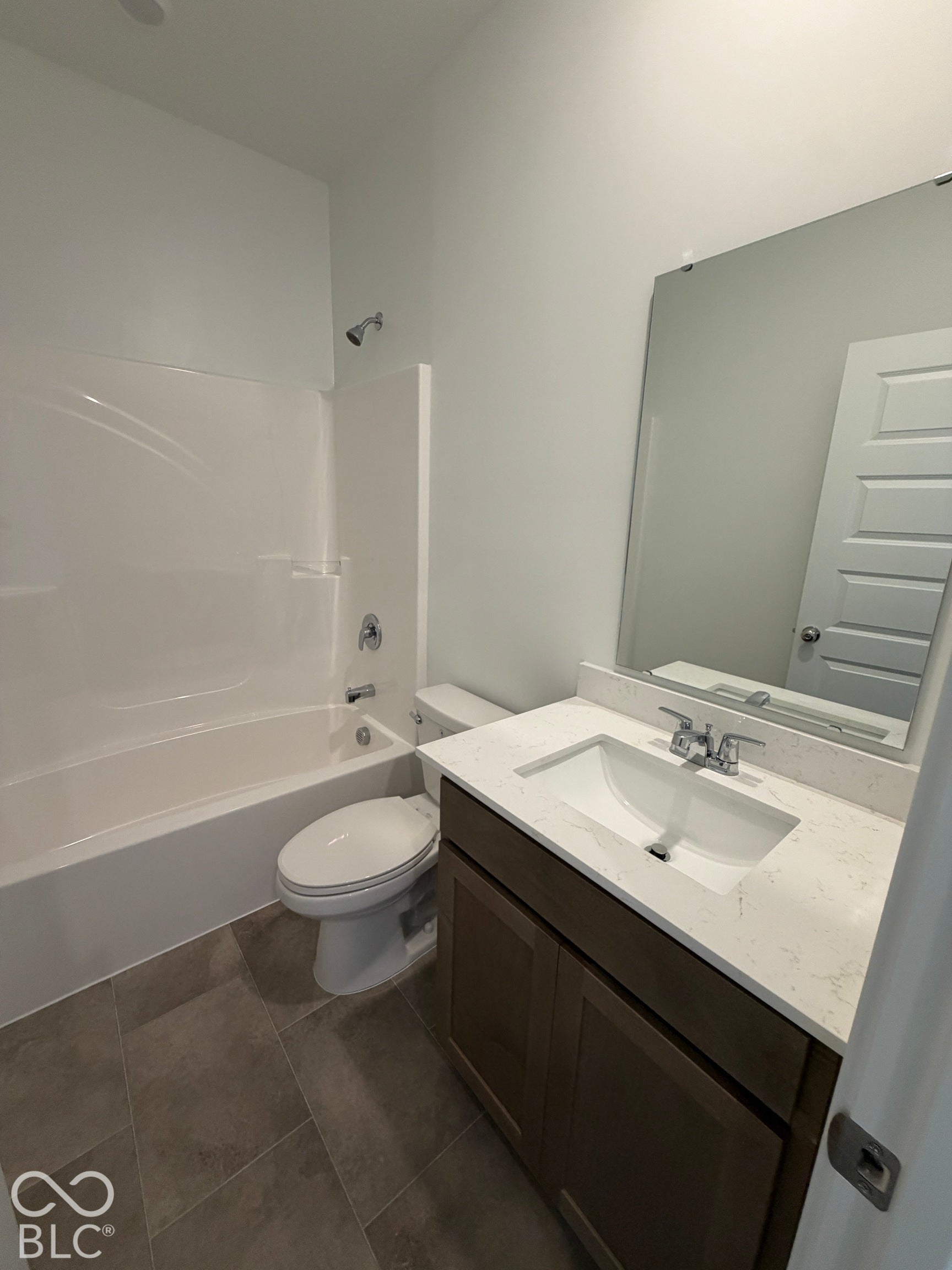 Bathroom featuring a single-sink vanity with a solid-surface countertop, dark wood-finish cabinetry, rectangular tile flooring, and a tub-shower combination with a surround