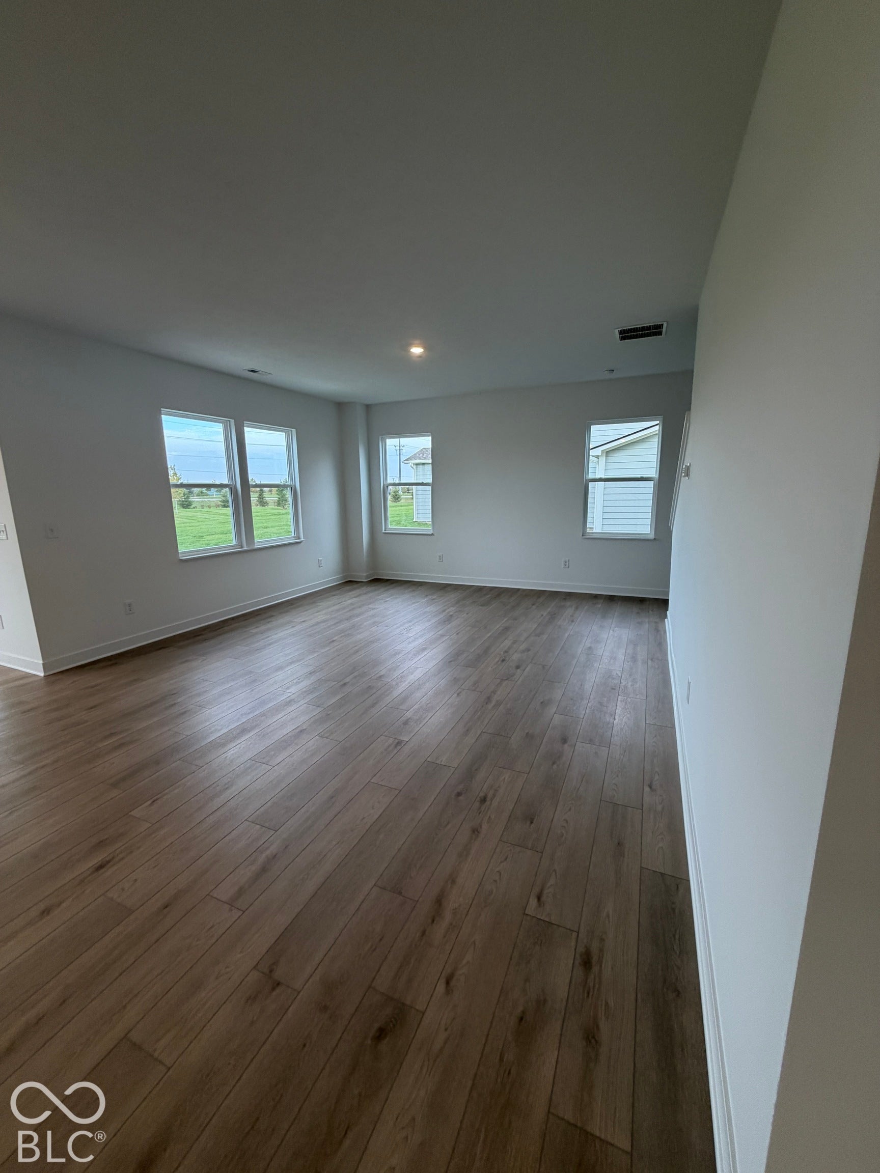 Open-concept room featuring neutral wall paint, wood-finish flooring, and multiple dual-pane windows