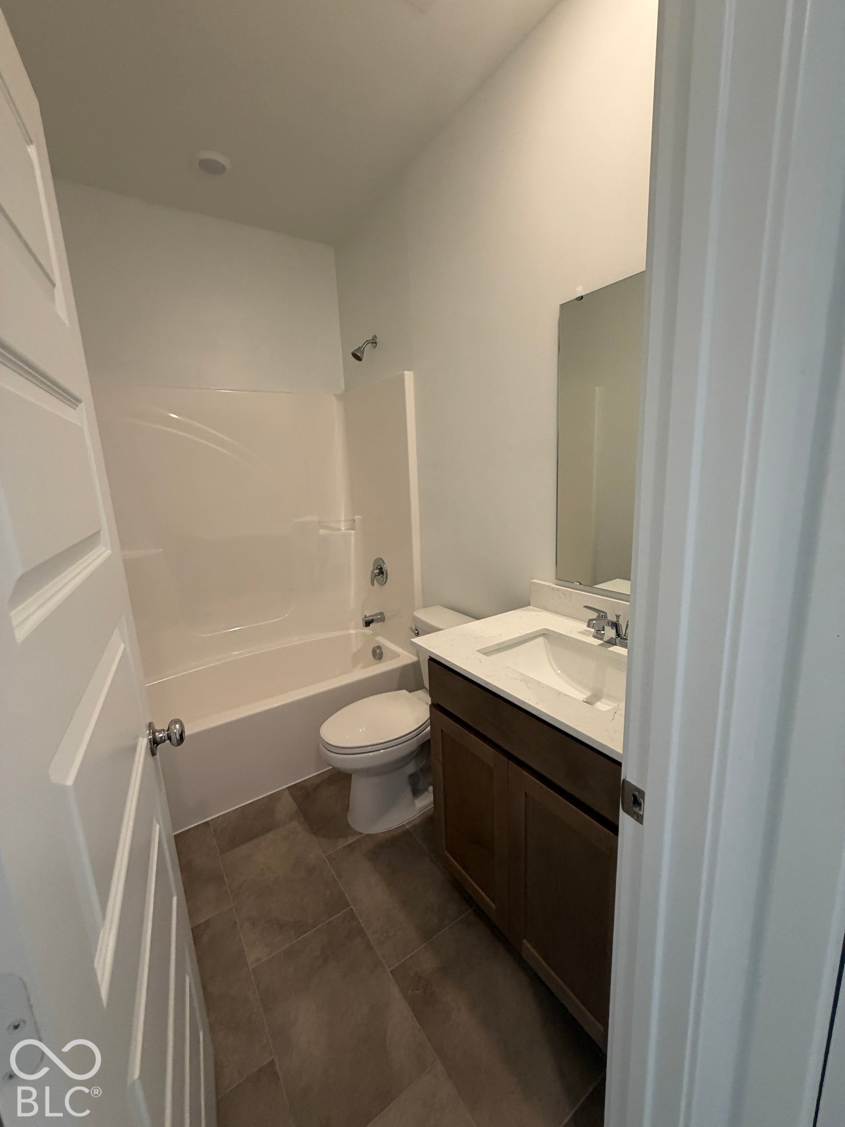 Bathroom featuring a bathtub with a white surround, vanity with dark-tone cabinetry, rectangular basin, white countertop, and neutral-toned tile flooring