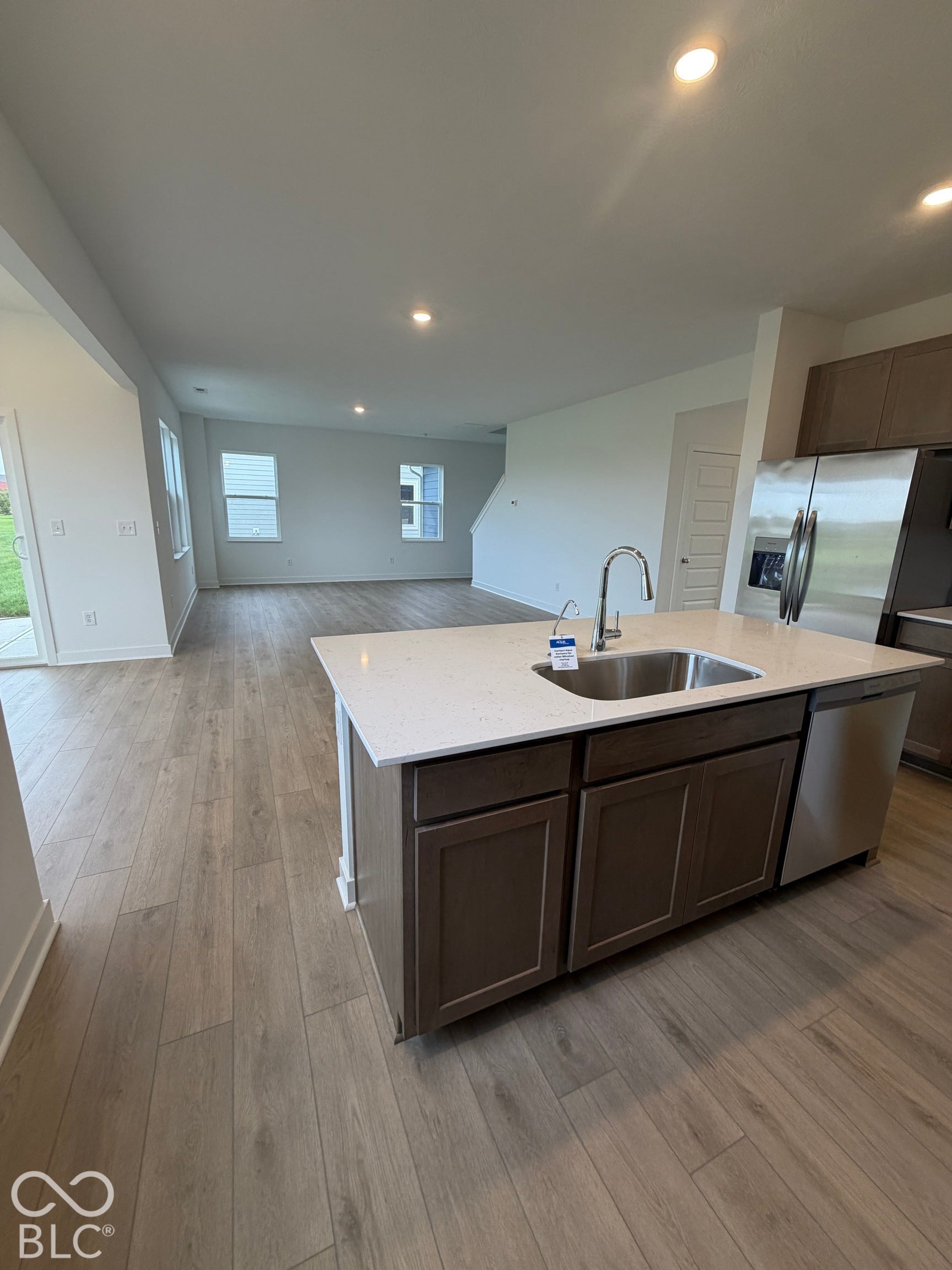 Kitchen island featuring a stone-composite countertop, stainless steel undermount sink with a gooseneck faucet, dark wood-finish cabinetry, stainless steel dishwasher, and wood-finish flooring