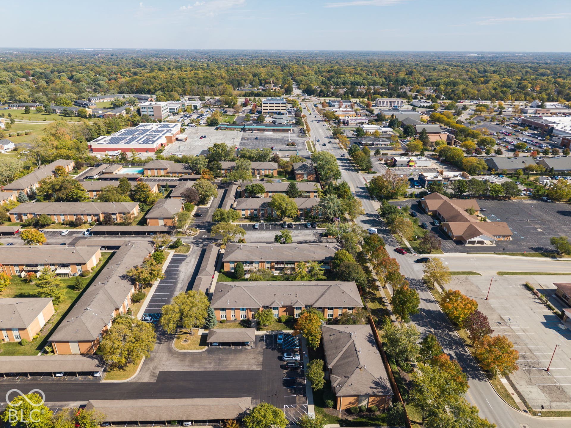Aerial perspective of the multi-building property featuring brick-exterior structures, shingled roofing, designated surface parking, and covered carports