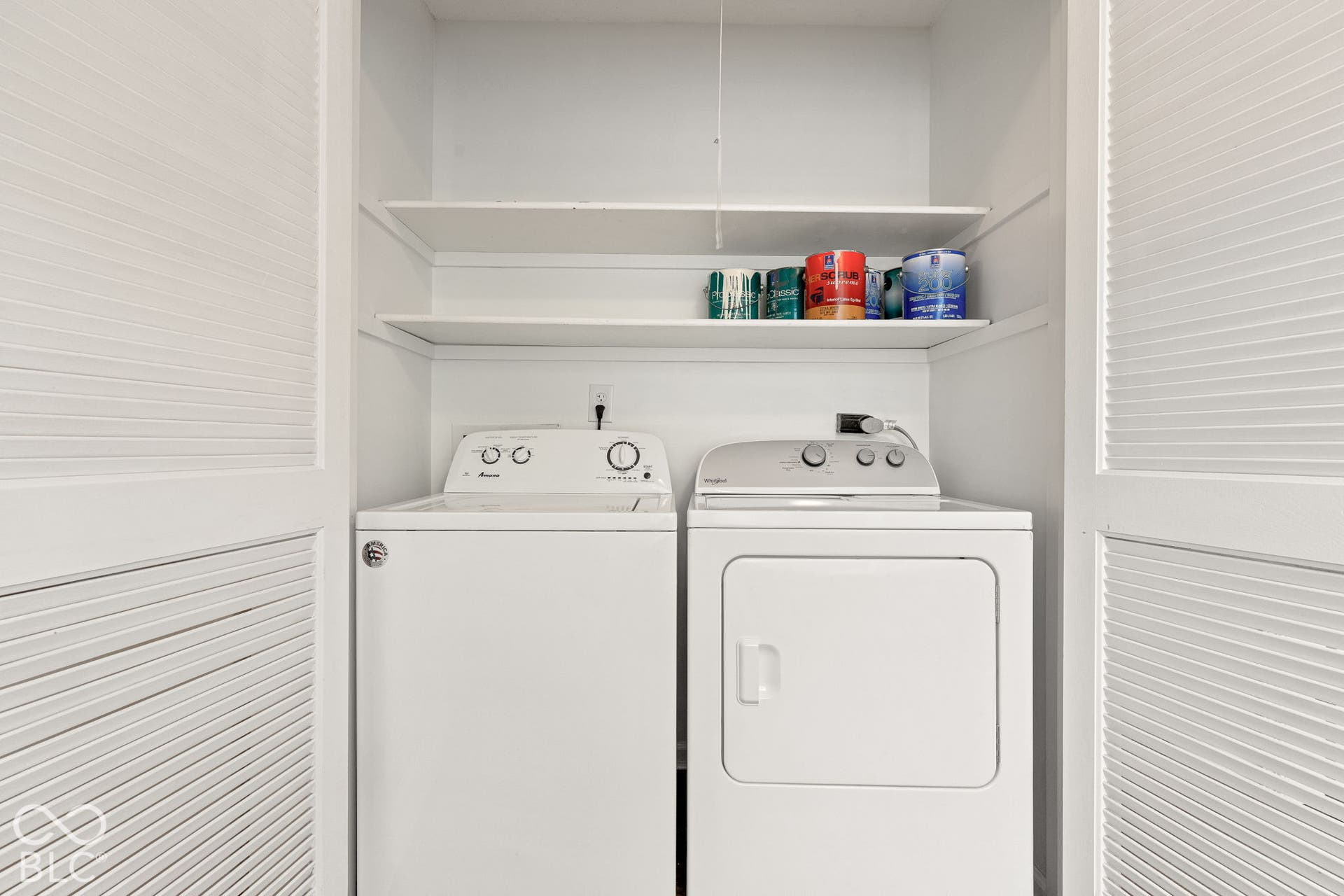 Laundry nook featuring white louvered bifold doors and dual open shelving