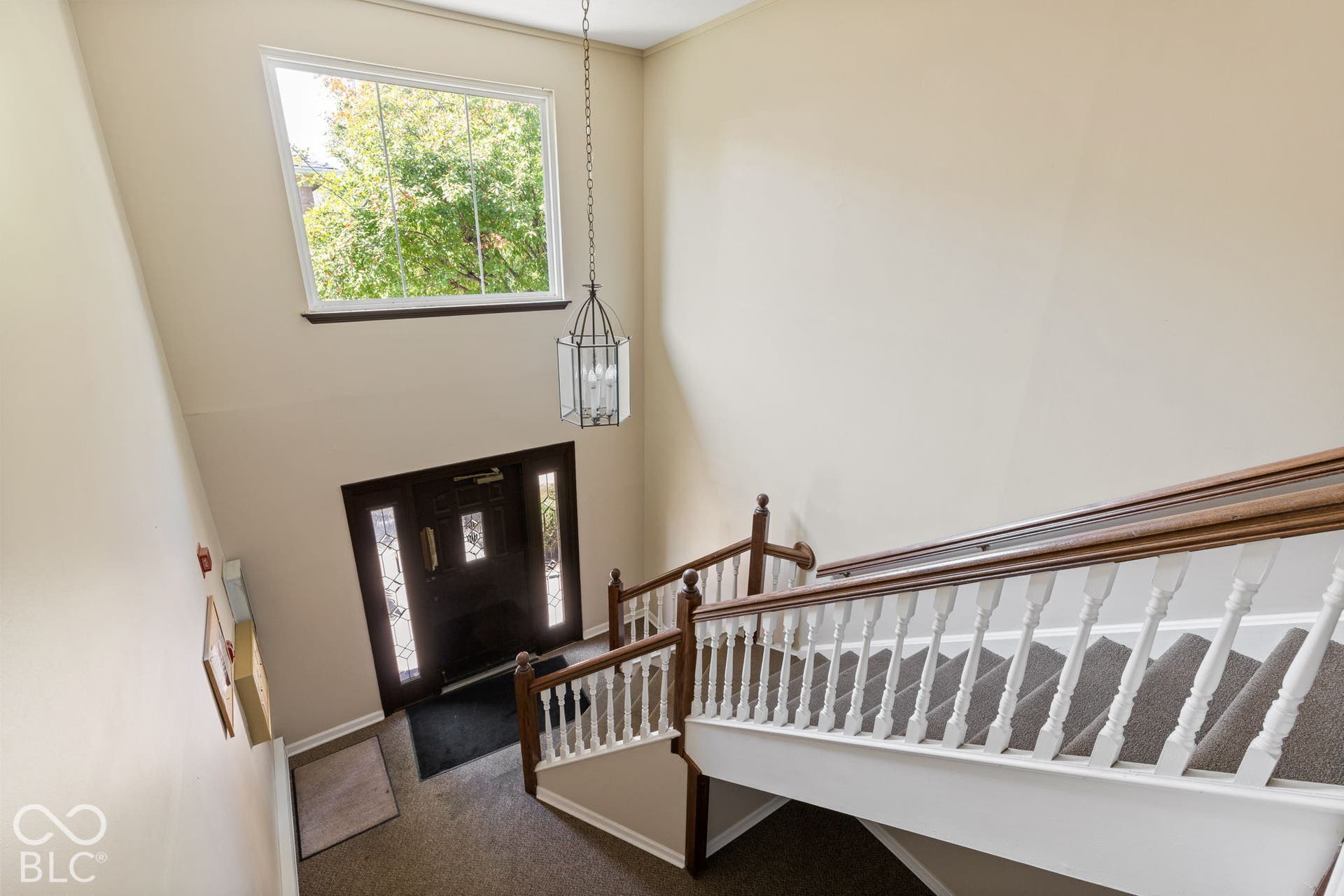 Double-height foyer featuring a multi-pane front door, overhead lantern-style pendant light, tall transom window, and staircase with a wood handrail and balusters