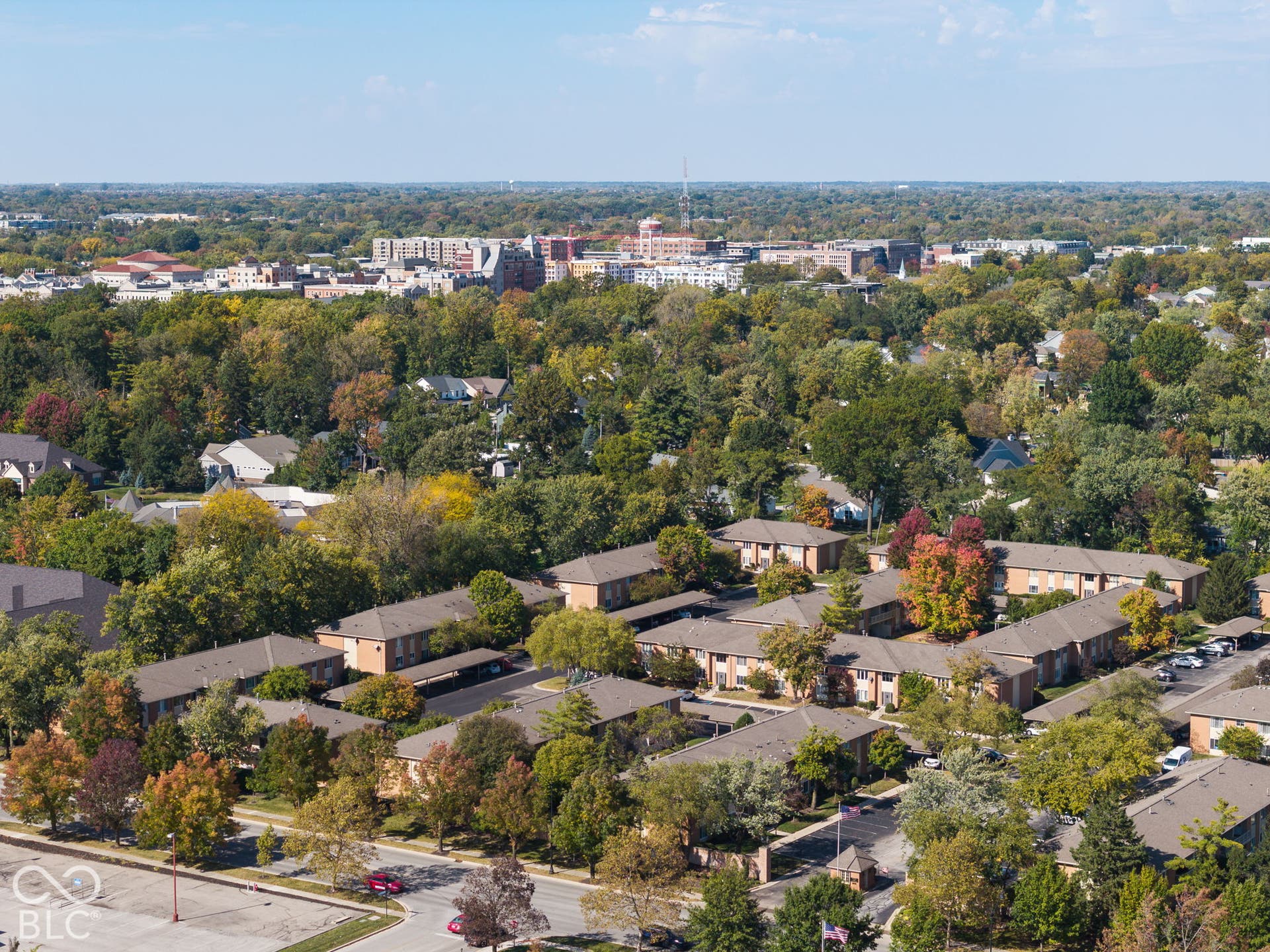Aerial perspective featuring multi-building residential complex, paved parking areas, covered carport structures, and mature tree canopy throughout the grounds