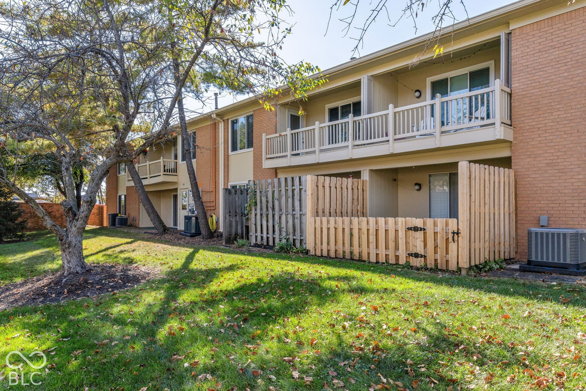 Multi-level exterior featuring brick masonry, second-story railed balconies, and private ground-level fenced patios