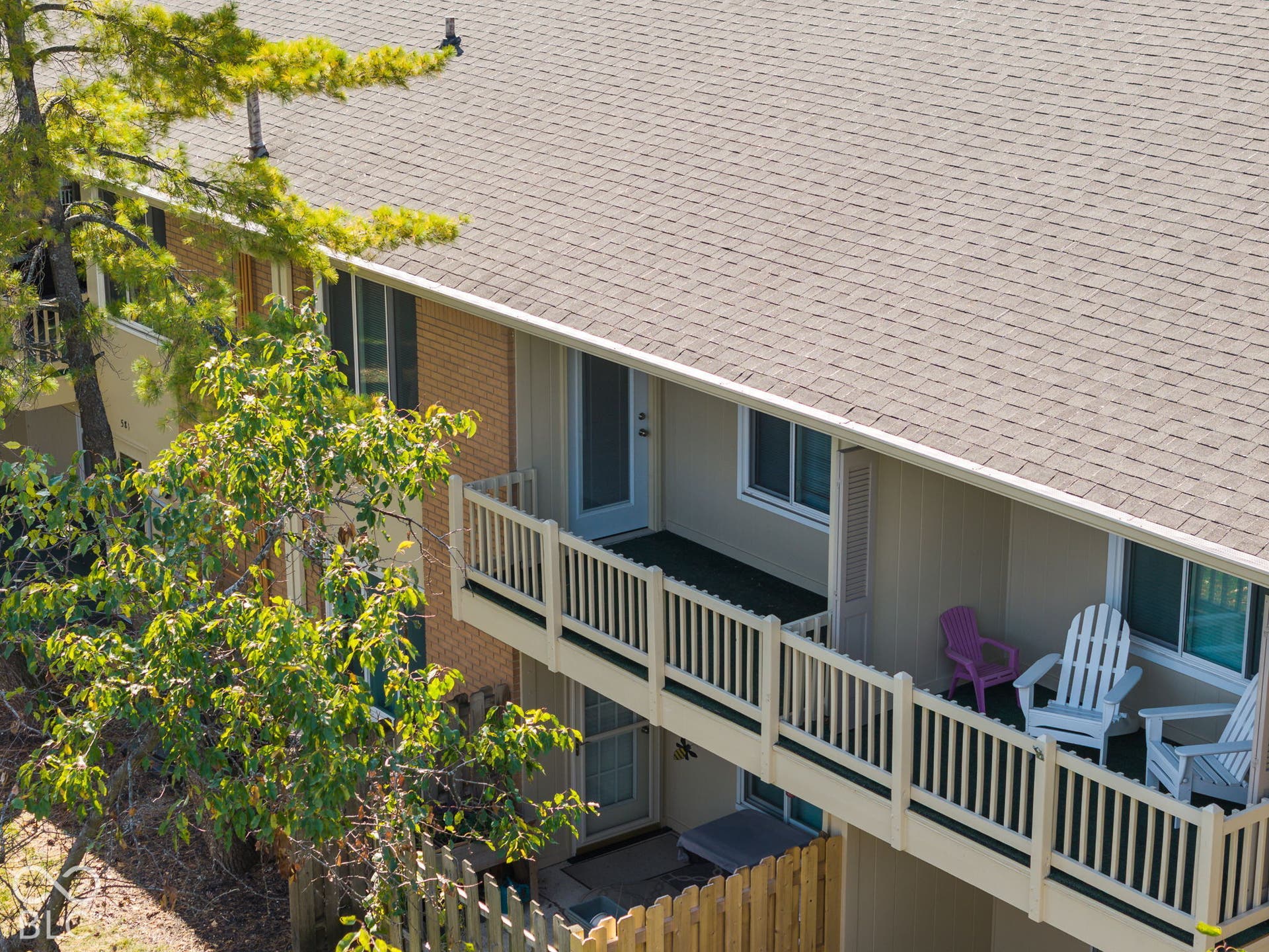 Exterior view featuring multi-level wood balconies with railing, light-toned horizontal siding, brick masonry accents, and an asphalt shingle roof
