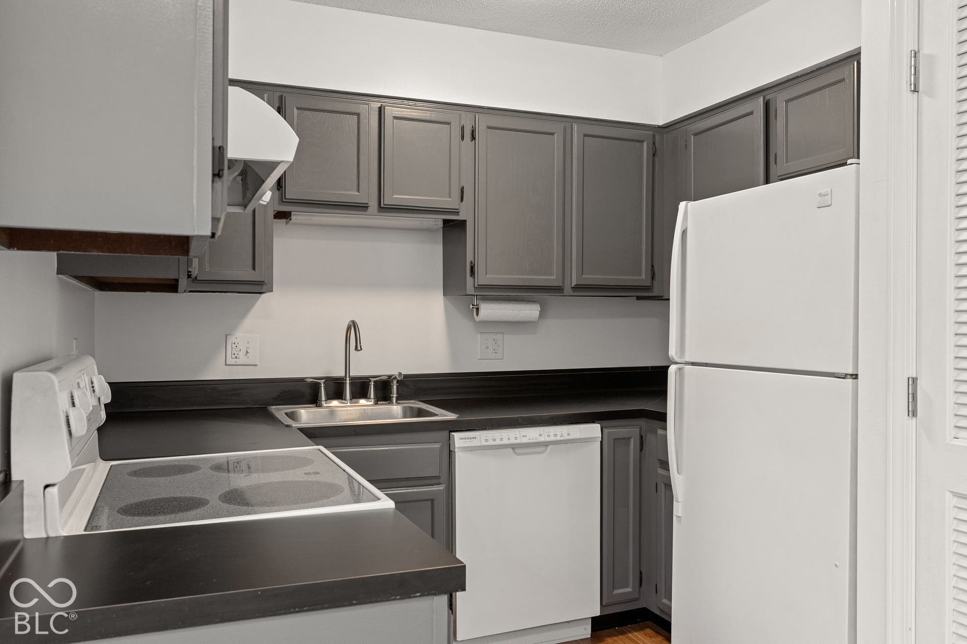 Kitchen featuring grey cabinetry, dark countertops, a stainless steel sink with a goose-neck faucet, and white appliances including an electric range, dishwasher, and refrigerator