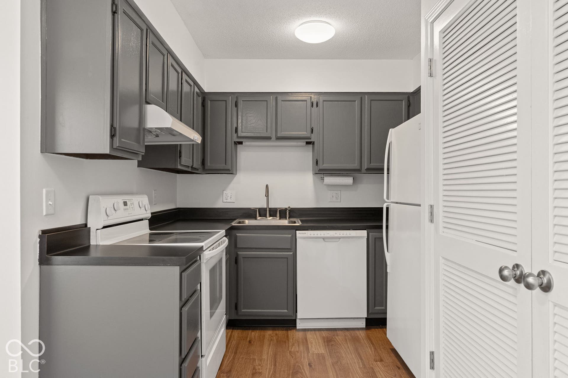 Kitchen featuring dark grey shaker-style cabinetry, charcoal laminate countertops, stainless steel sink, and wood-finish flooring