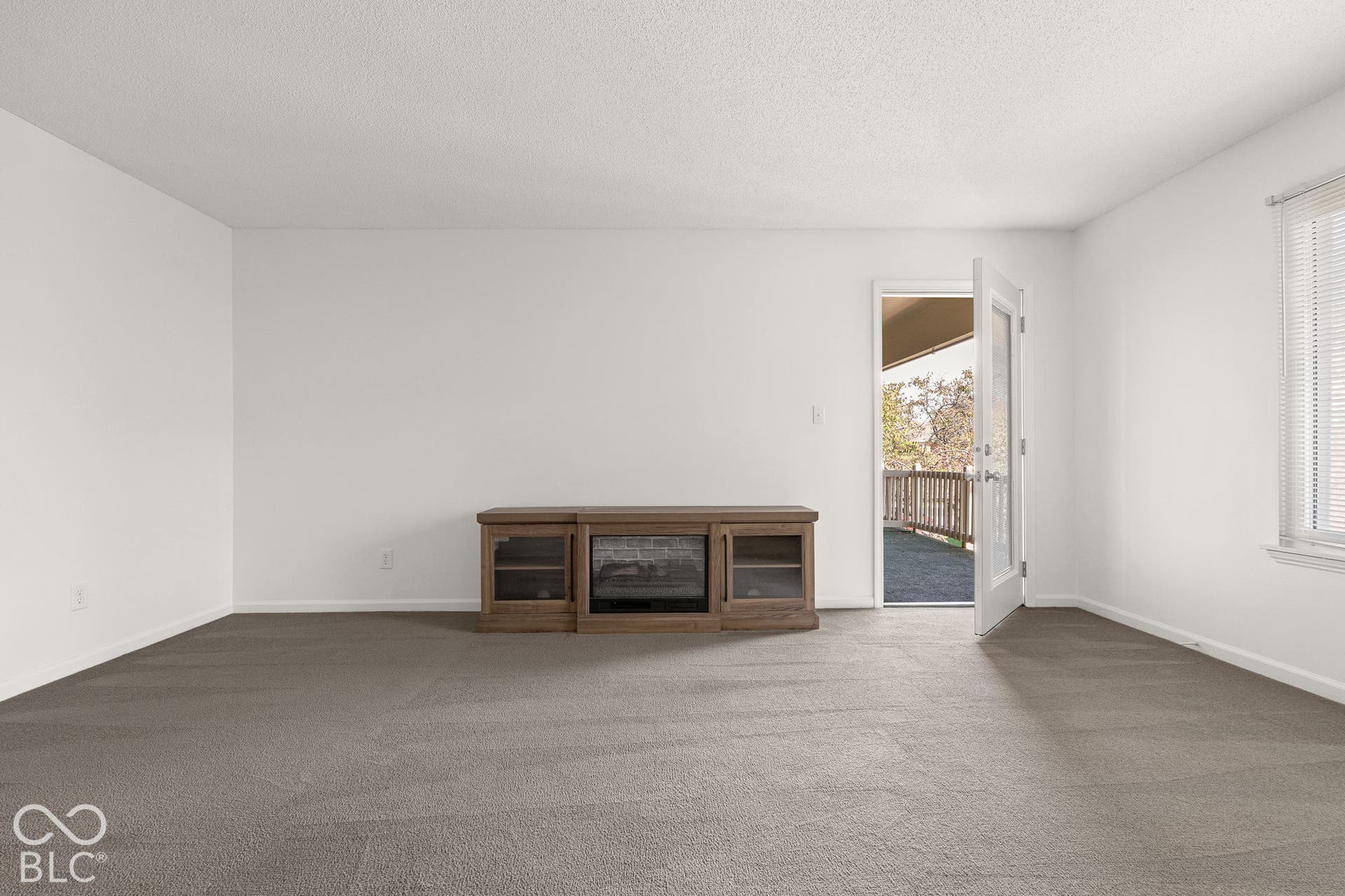 Interior space featuring neutral-toned carpeting, white walls, a built-in wood-finish electric fireplace console, and a glass-paneled exterior door