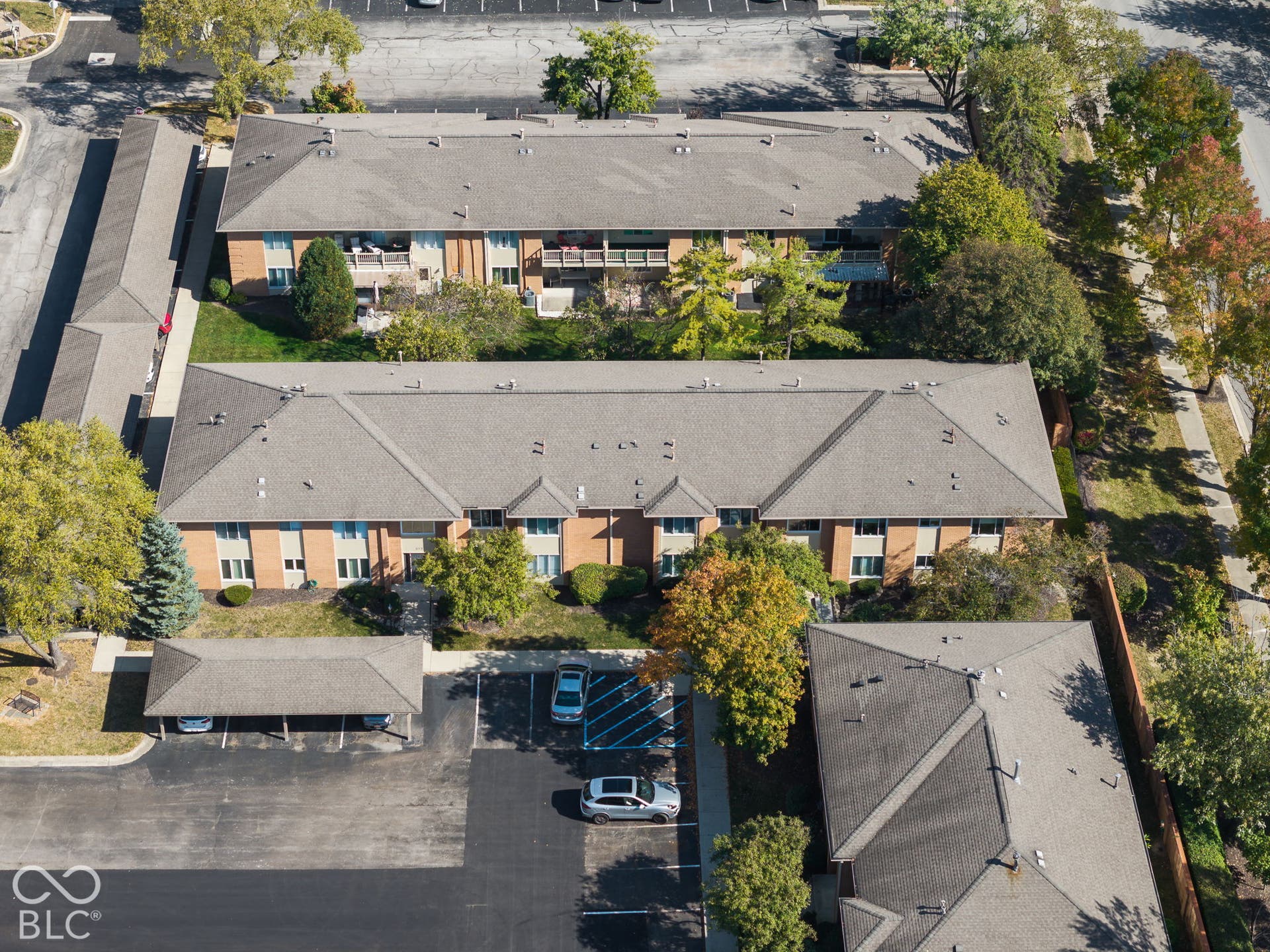 Aerial view of brick exterior multi-family buildings featuring asphalt shingle roofing, paved surface parking lots, and covered parking carports