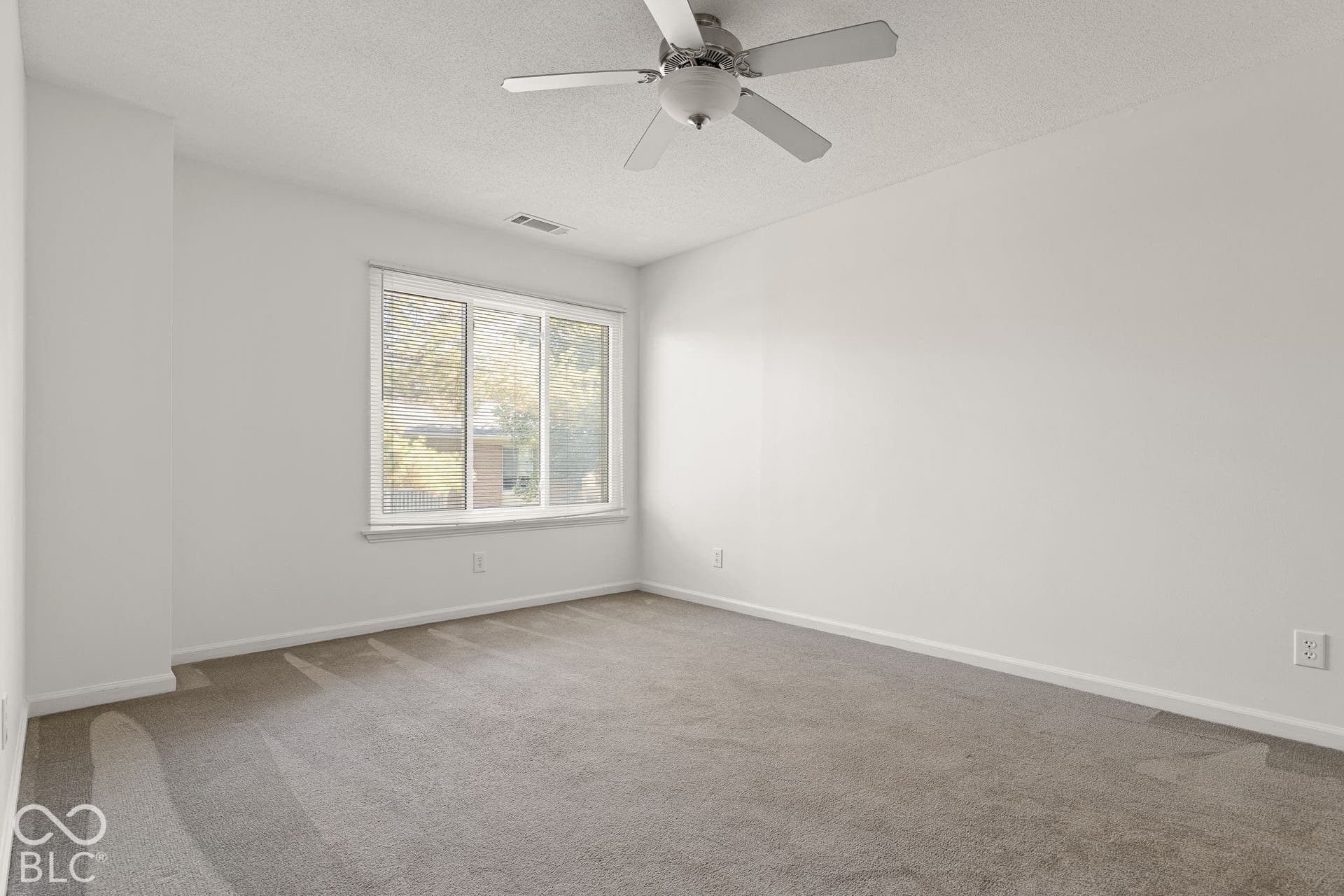Neutral interior space featuring wall-to-wall carpeting, a multi-pane sliding window, and a central white ceiling fan with integrated light fixture