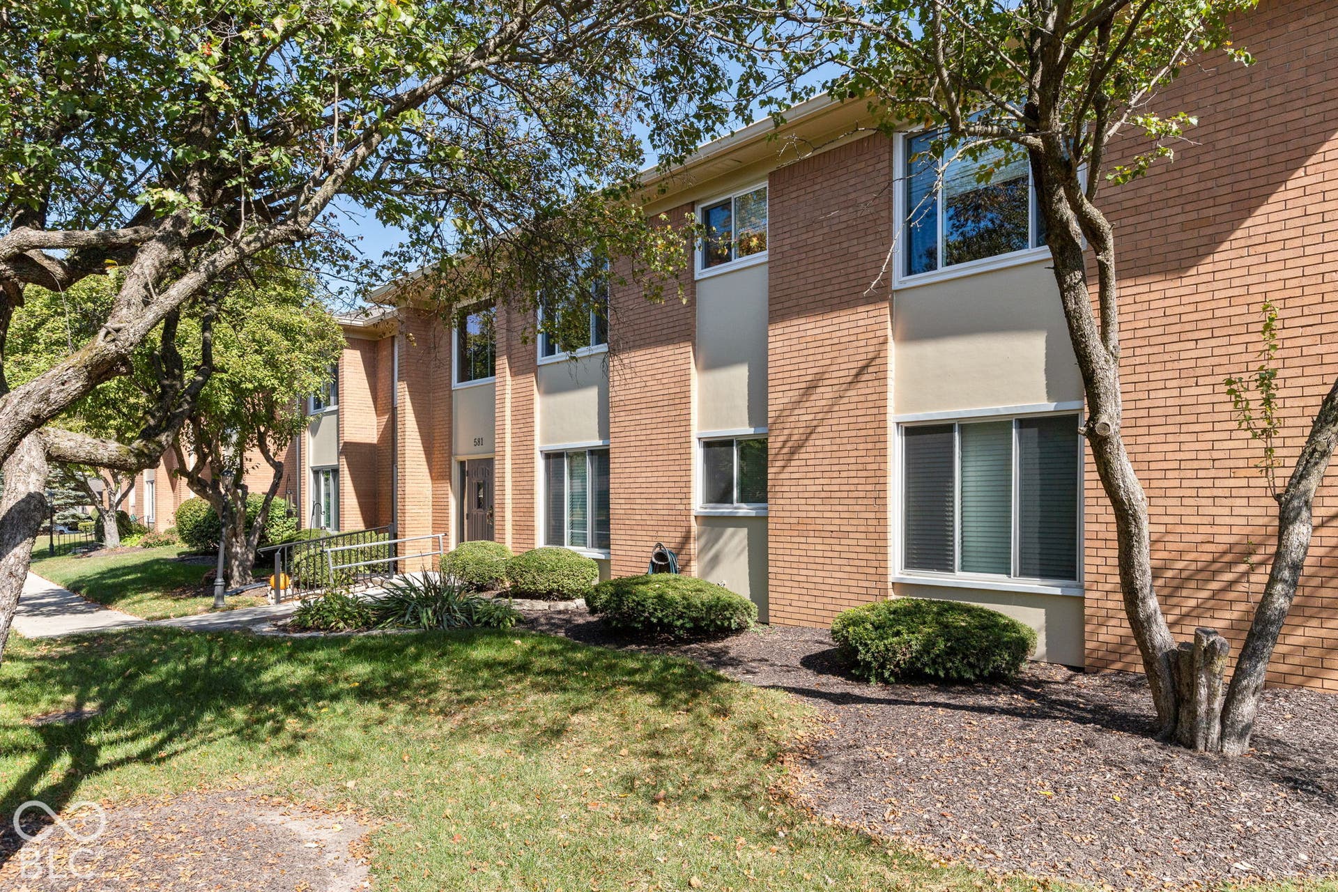 Multi-story brick exterior featuring light-toned smooth masonry accents, dual-pane windows, and a paved exterior pathway with metal handrails