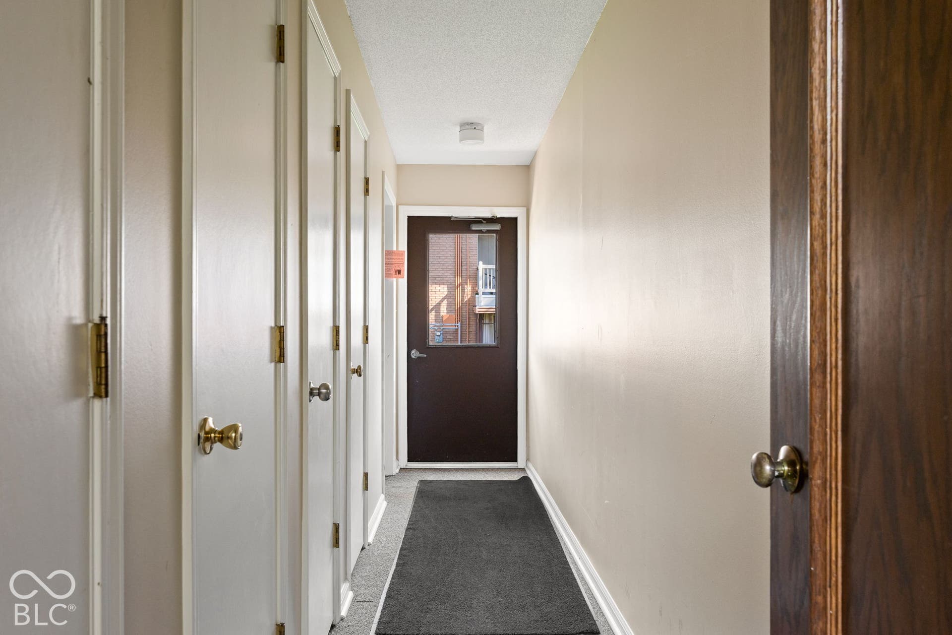 Hallway featuring multiple closet doors with brass-tone hardware, textured ceiling, and exterior-facing door with a glass insert