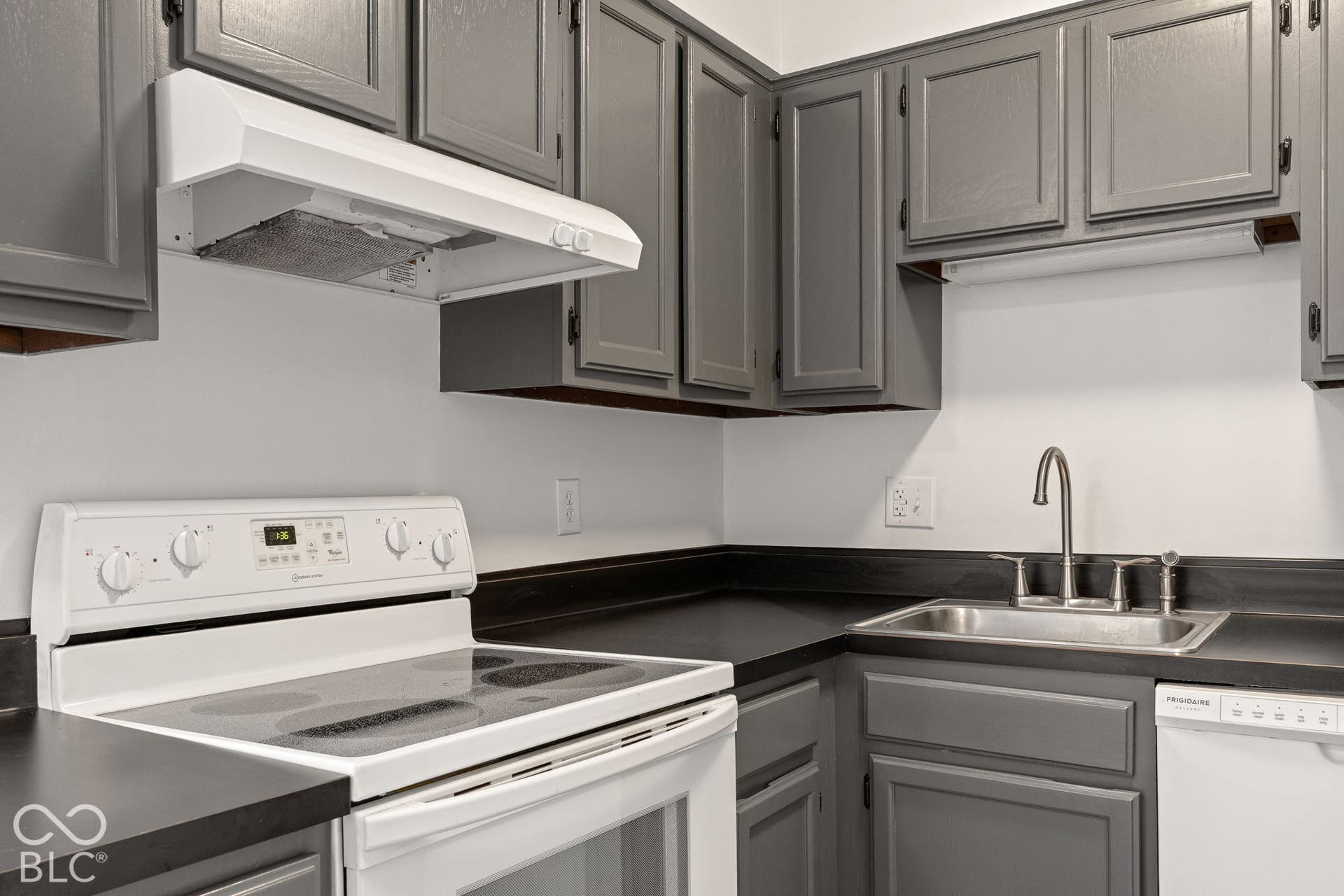 Kitchen featuring grey shaker-style cabinetry, matte black countertops, a stainless steel sink with a high-arch faucet, and white appliances