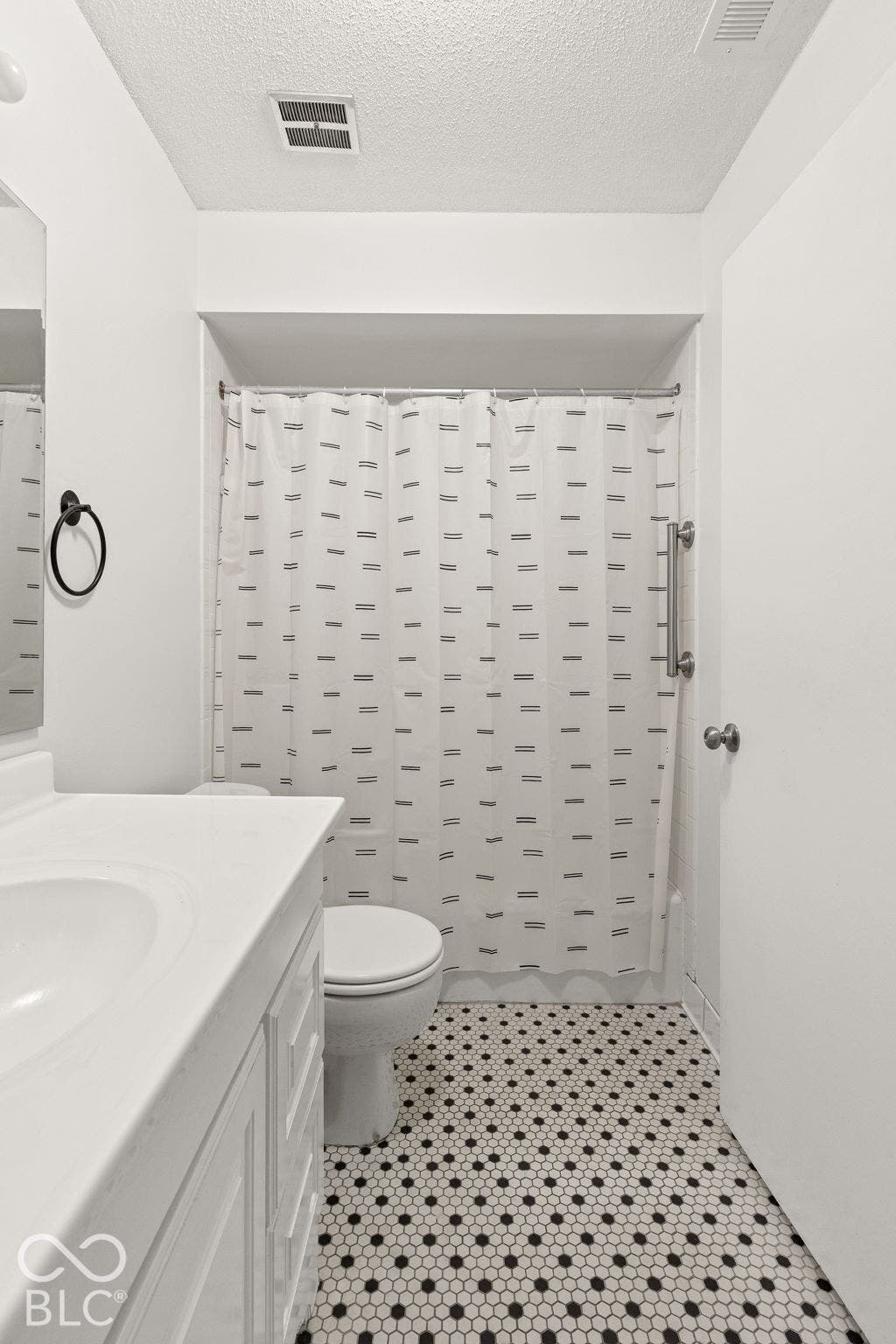 Bathroom featuring white cabinetry, integrated sink, black and white hexagonal floor tile, and a wall-mounted support bar