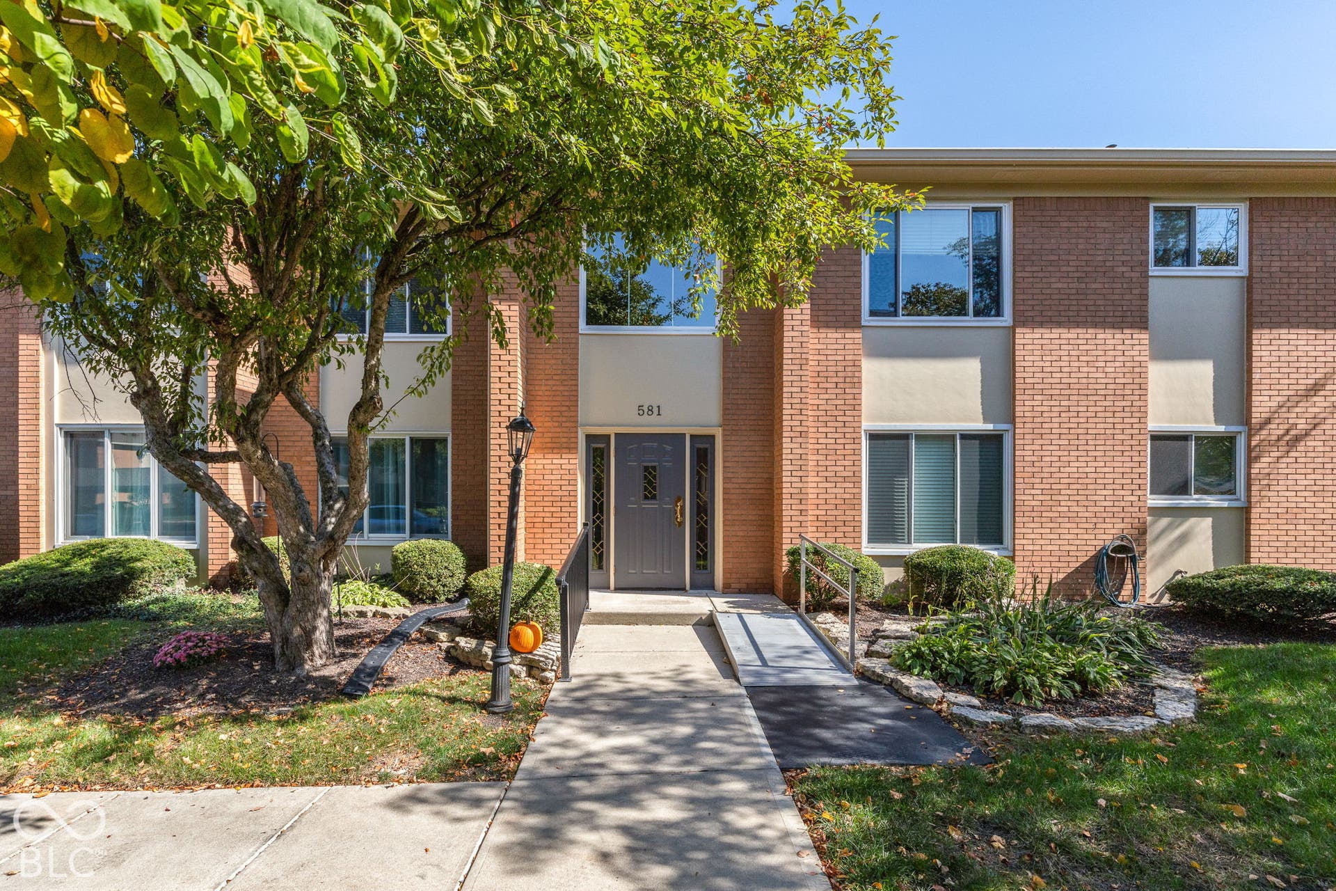 Brick exterior facade featuring a concrete walkway, exterior lamp post, and metal access ramp