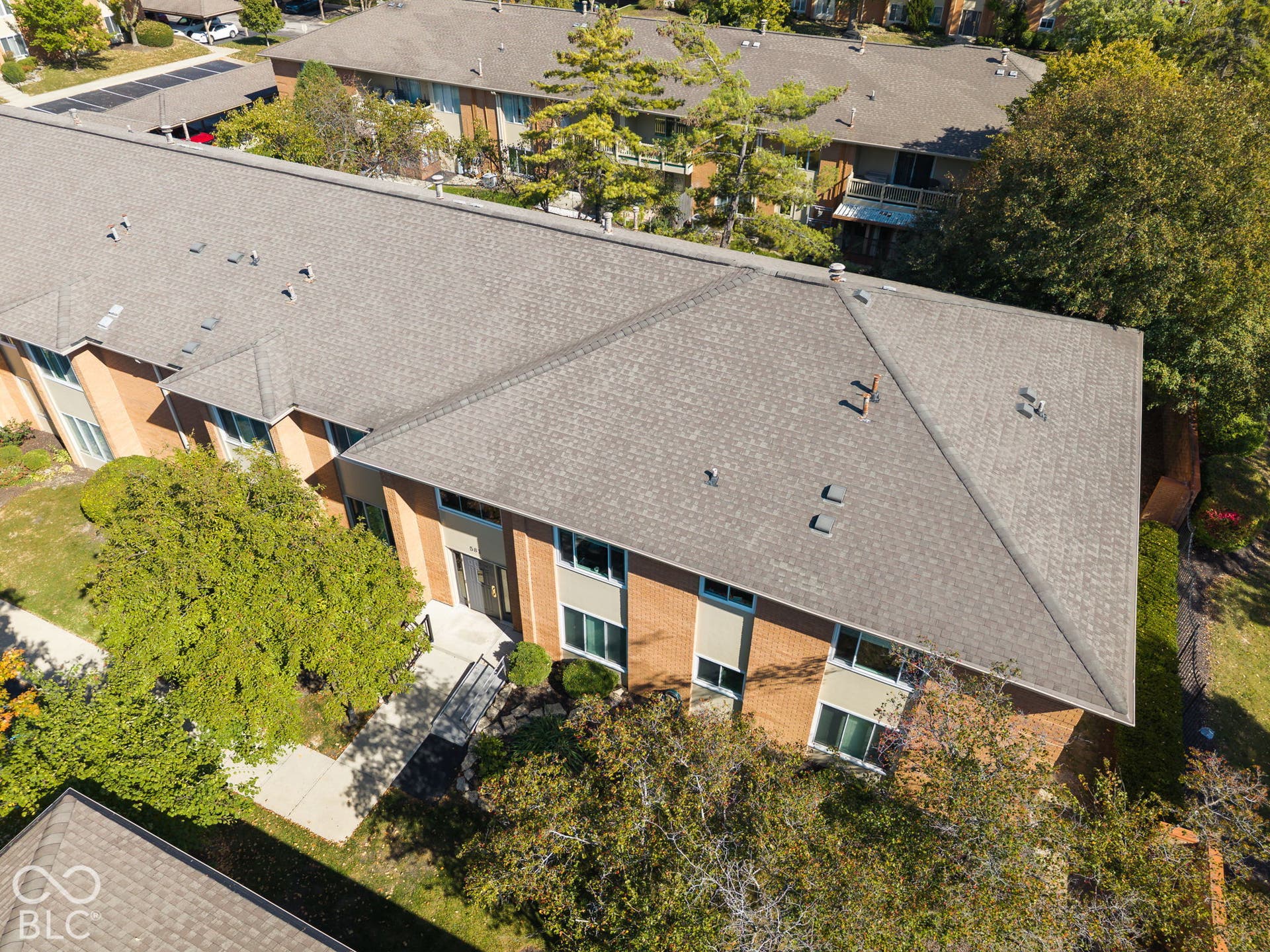 Multi-story brick exterior building featuring a multi-gabled shingle roof, concrete walkways, and mature landscaping
