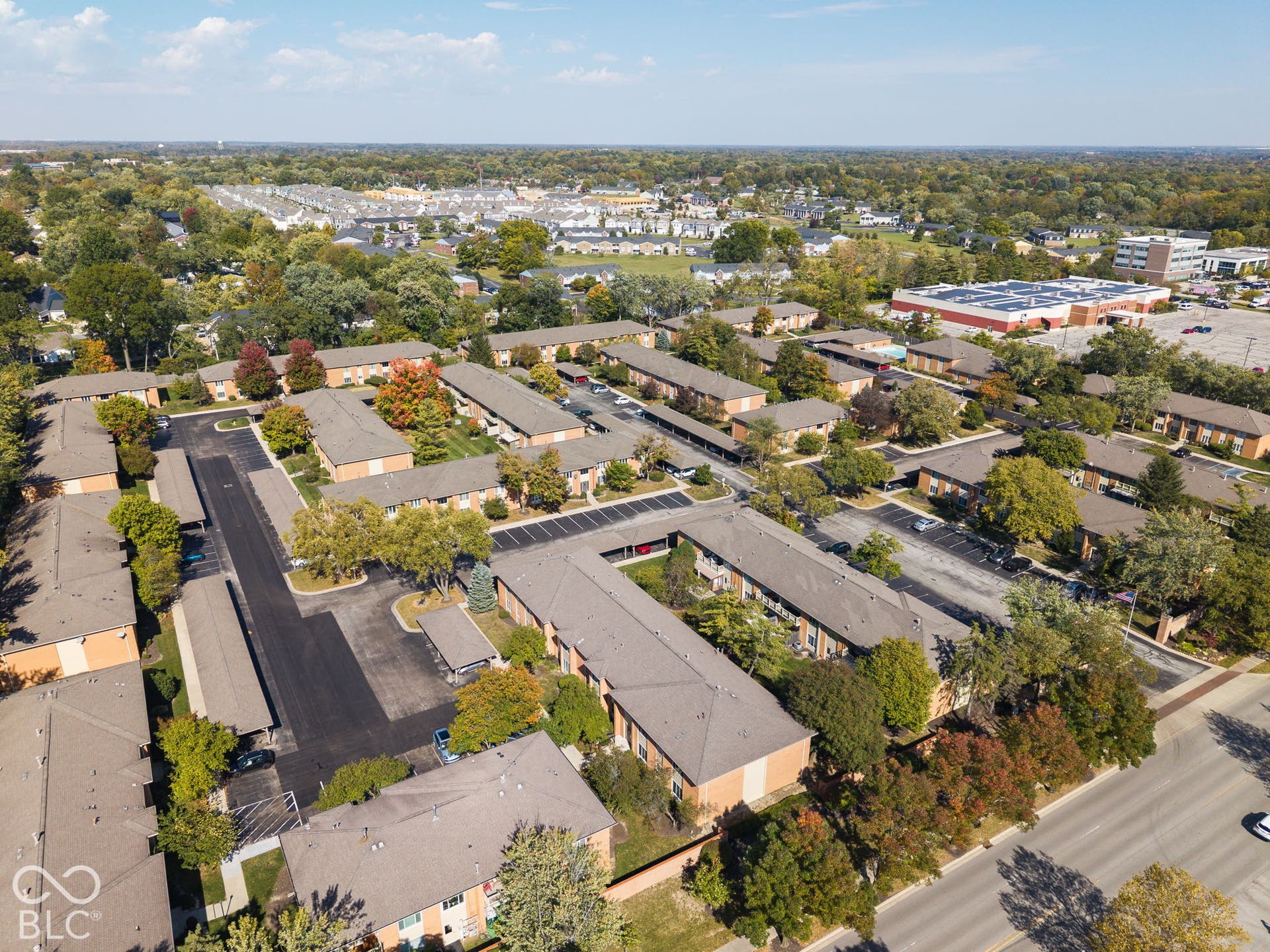 Multi-building residential complex featuring asphalt parking lots, covered parking structures, mature trees, and landscaped grounds
