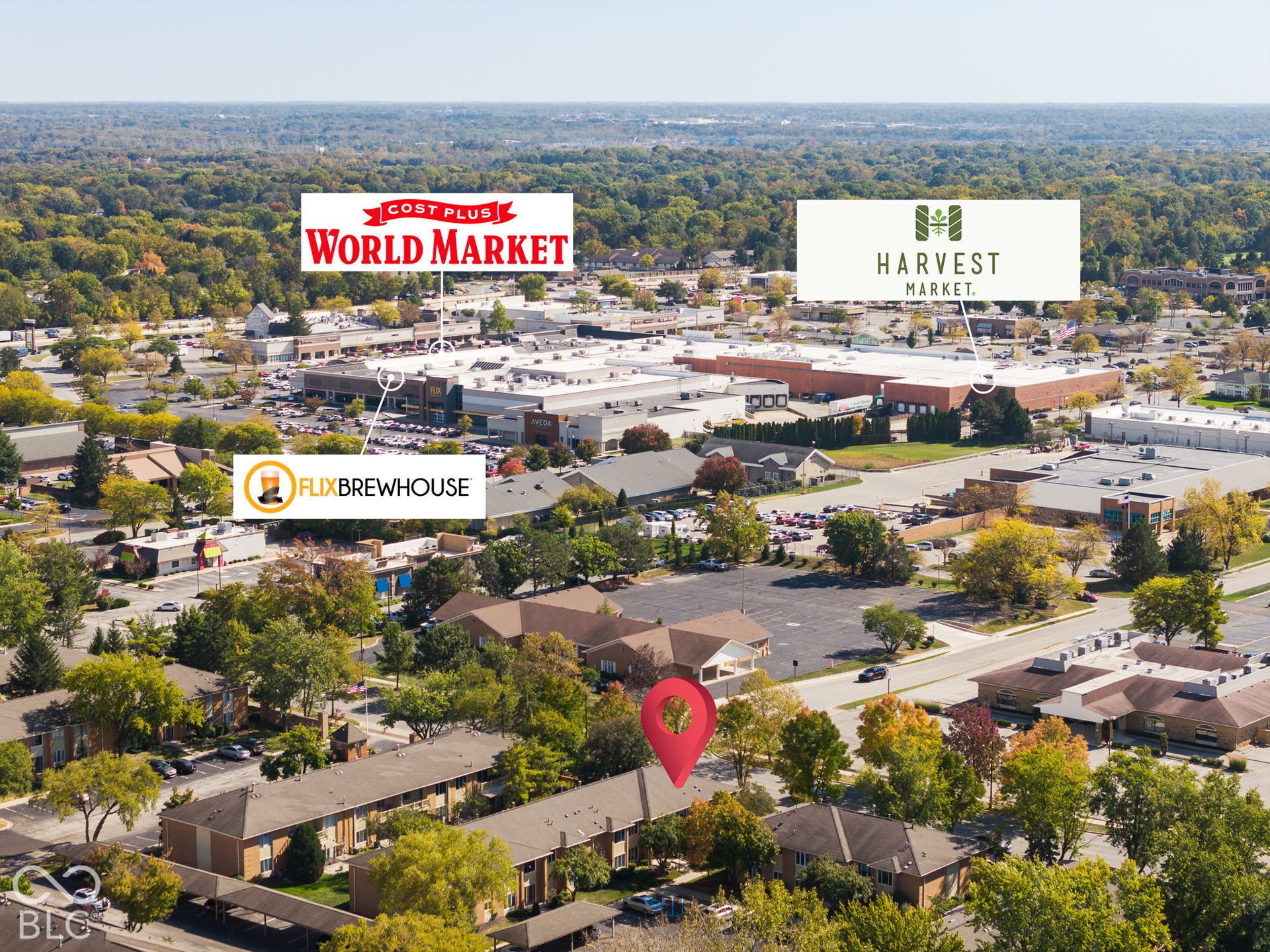 Aerial perspective featuring multi-unit residential structures with attached covered parking, surrounded by mature trees and proximity to commercial retail centers