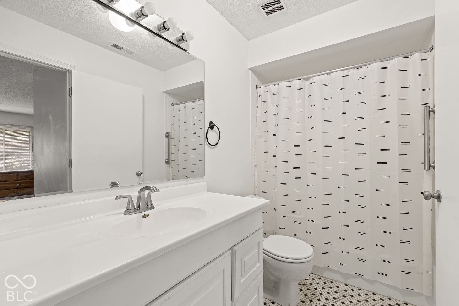 Bathroom featuring a white vanity with integrated sink, polished chrome faucet, expansive wall-mounted mirror with multi-light fixture, and mosaic-patterned tile flooring