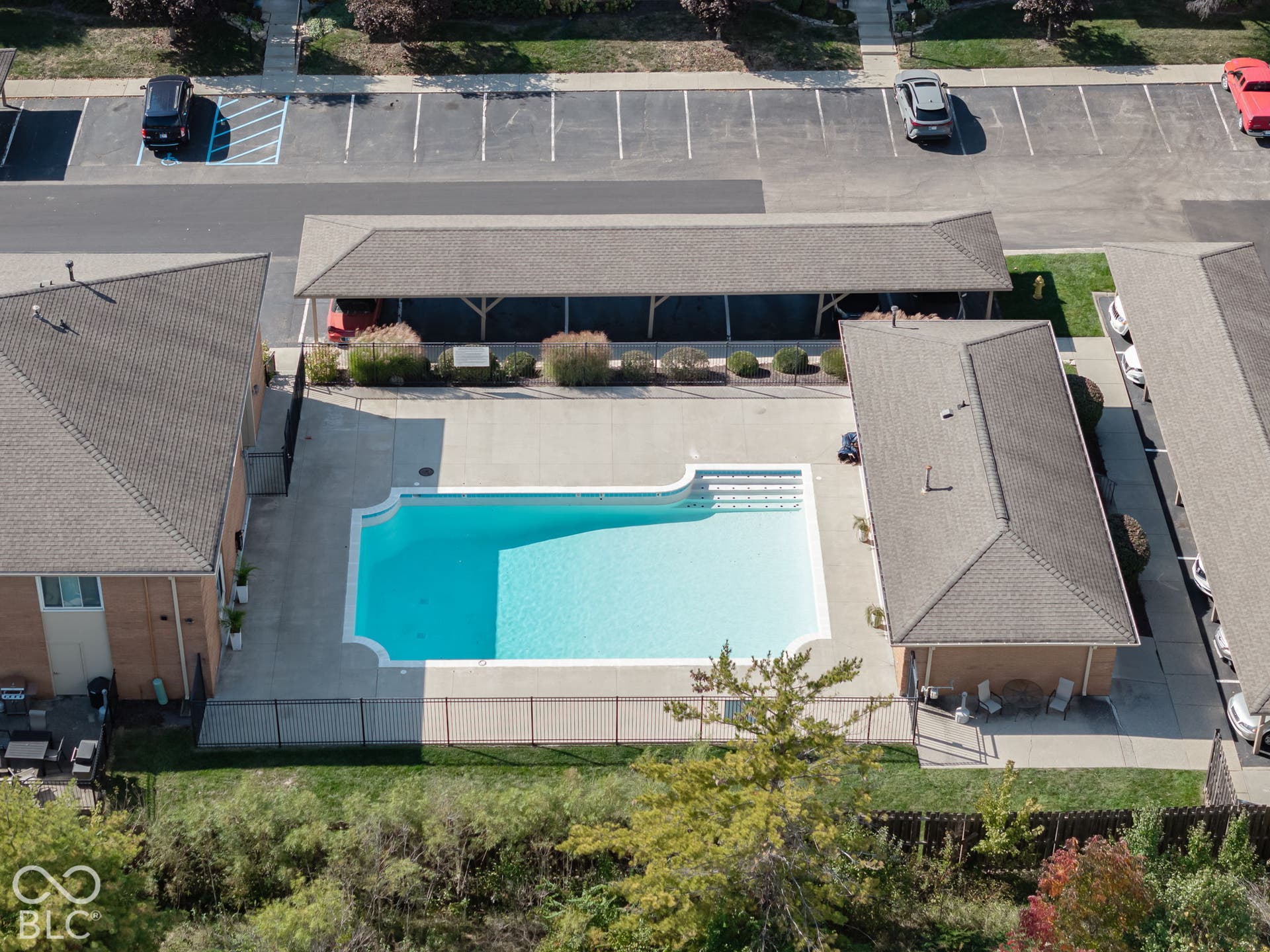 In-ground swimming pool featuring a concrete deck, built-in steps, and a metal perimeter fence, complemented by a covered parking structure