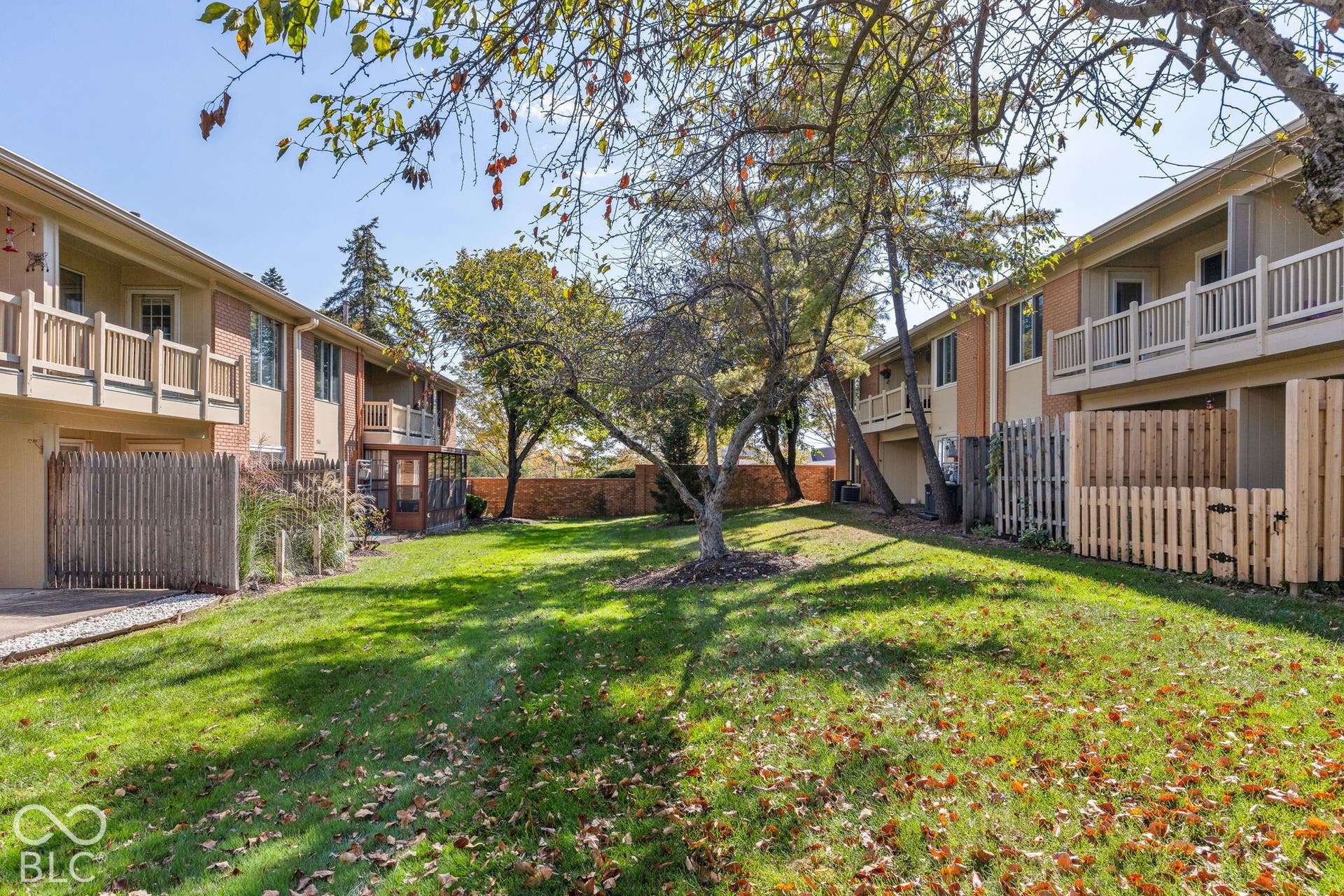 Common area featuring a grass lawn, mature trees, wood-slat privacy fencing, and exterior balconies