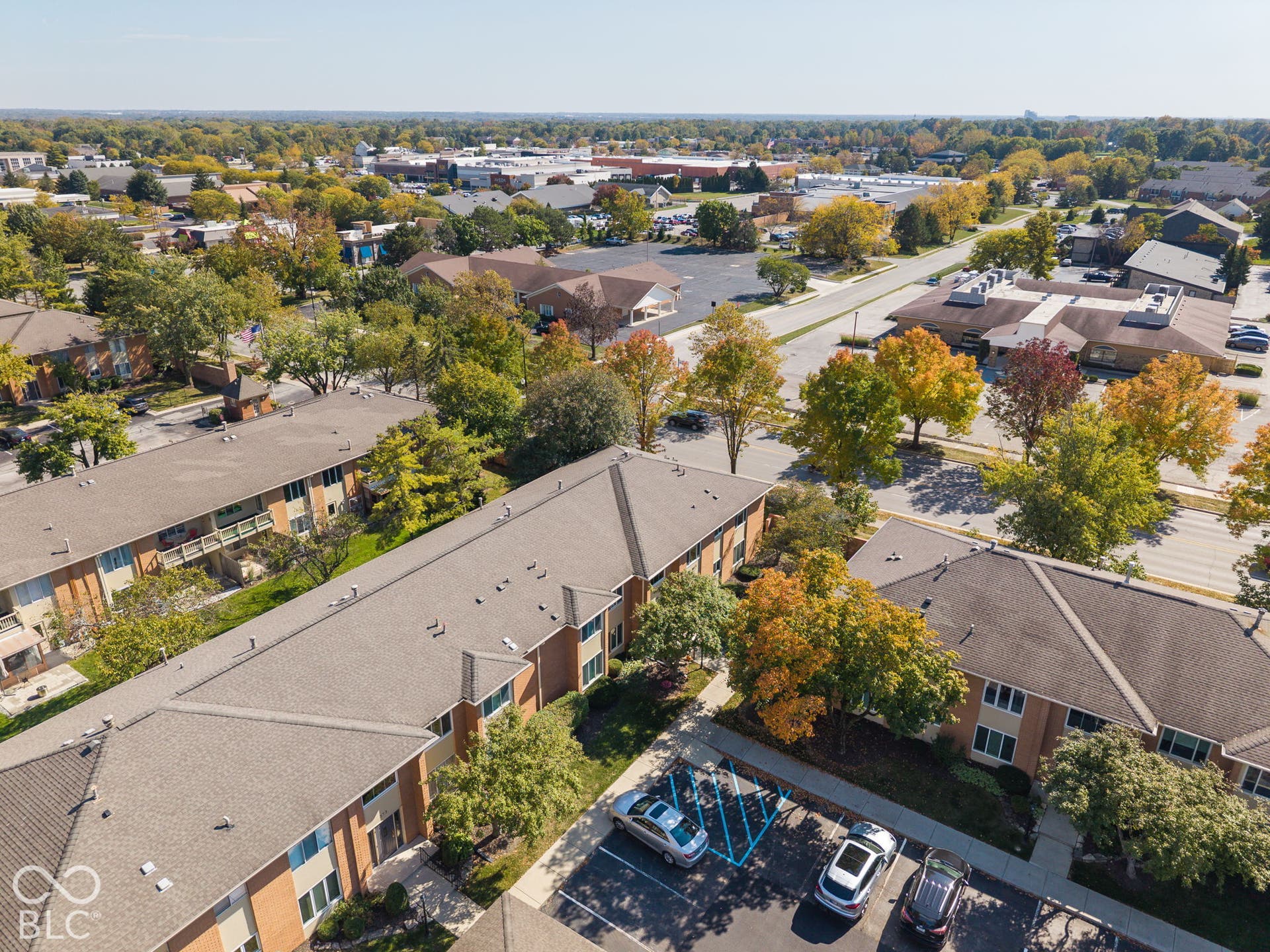 Aerial perspective of multi-family brick structures featuring asphalt shingle roofing, paved surface parking areas, and mature landscaping
