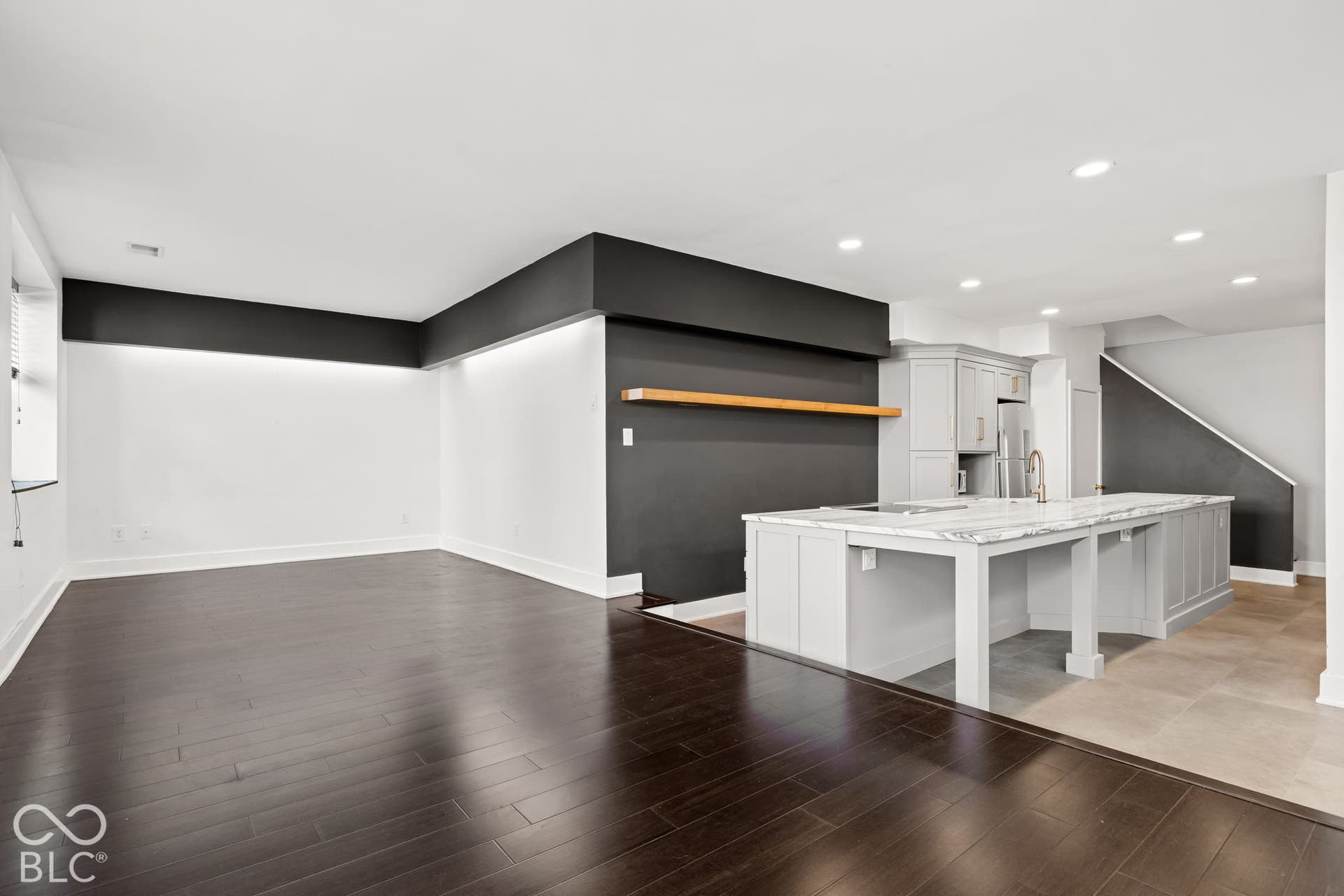 Open floor plan featuring wood-finish flooring, a kitchen island with stone-finish countertops, recessed lighting, and a floating wood wall shelf