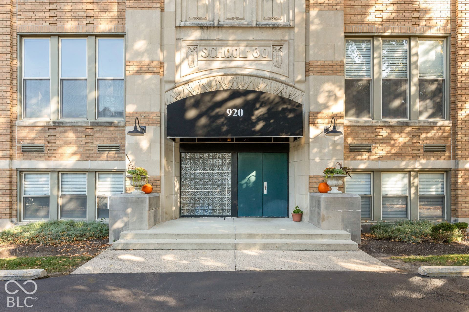Historic brick exterior featuring decorative stone masonry, arched entryway detailing, a solid metal door, glass block paneling, and an expansive concrete staircase