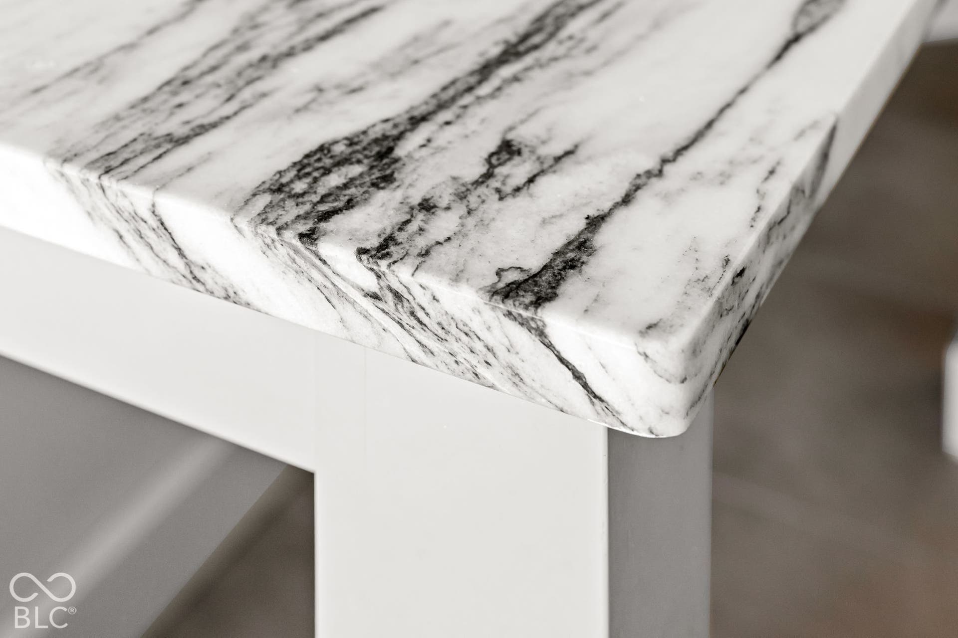 Stone countertop featuring a polished finish, high-contrast veining, and a rounded eased edge, supported by a solid white base