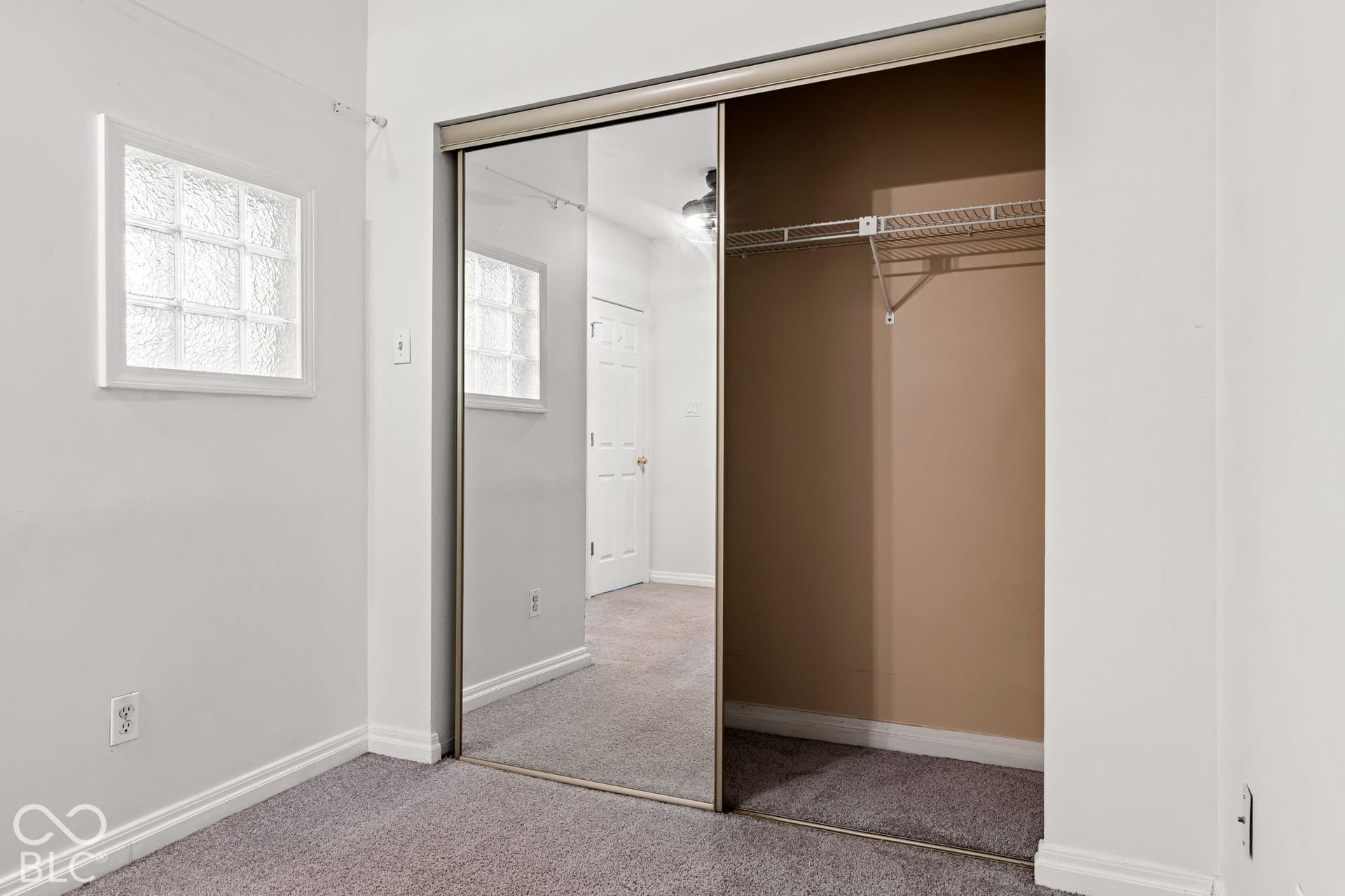 Closet featuring mirrored sliding doors, interior wire shelving, glass block accent window, and carpeting