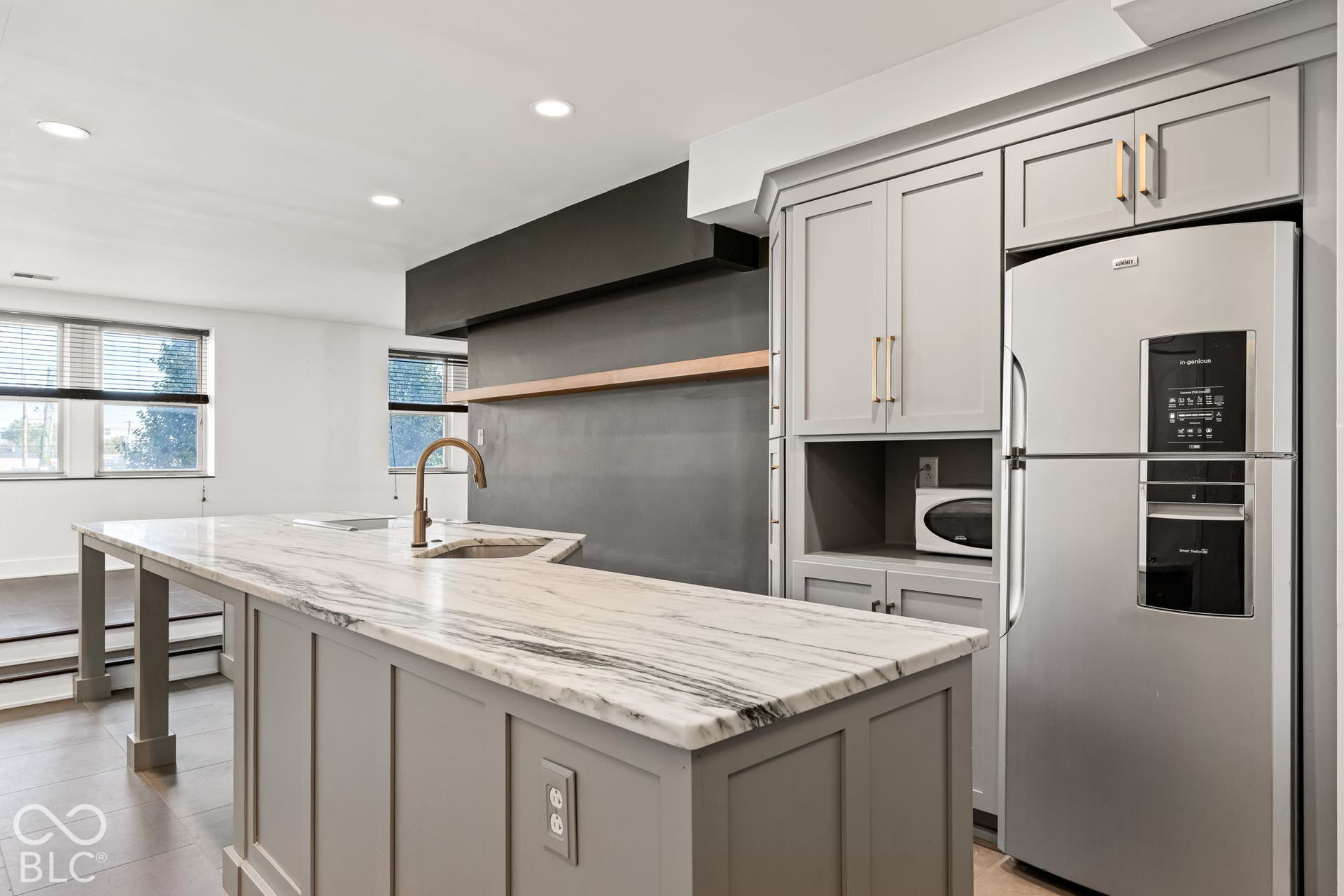 Kitchen featuring an island with stone-finish countertops, grey cabinetry with brass-tone hardware, stainless steel refrigerator, and recessed lighting
