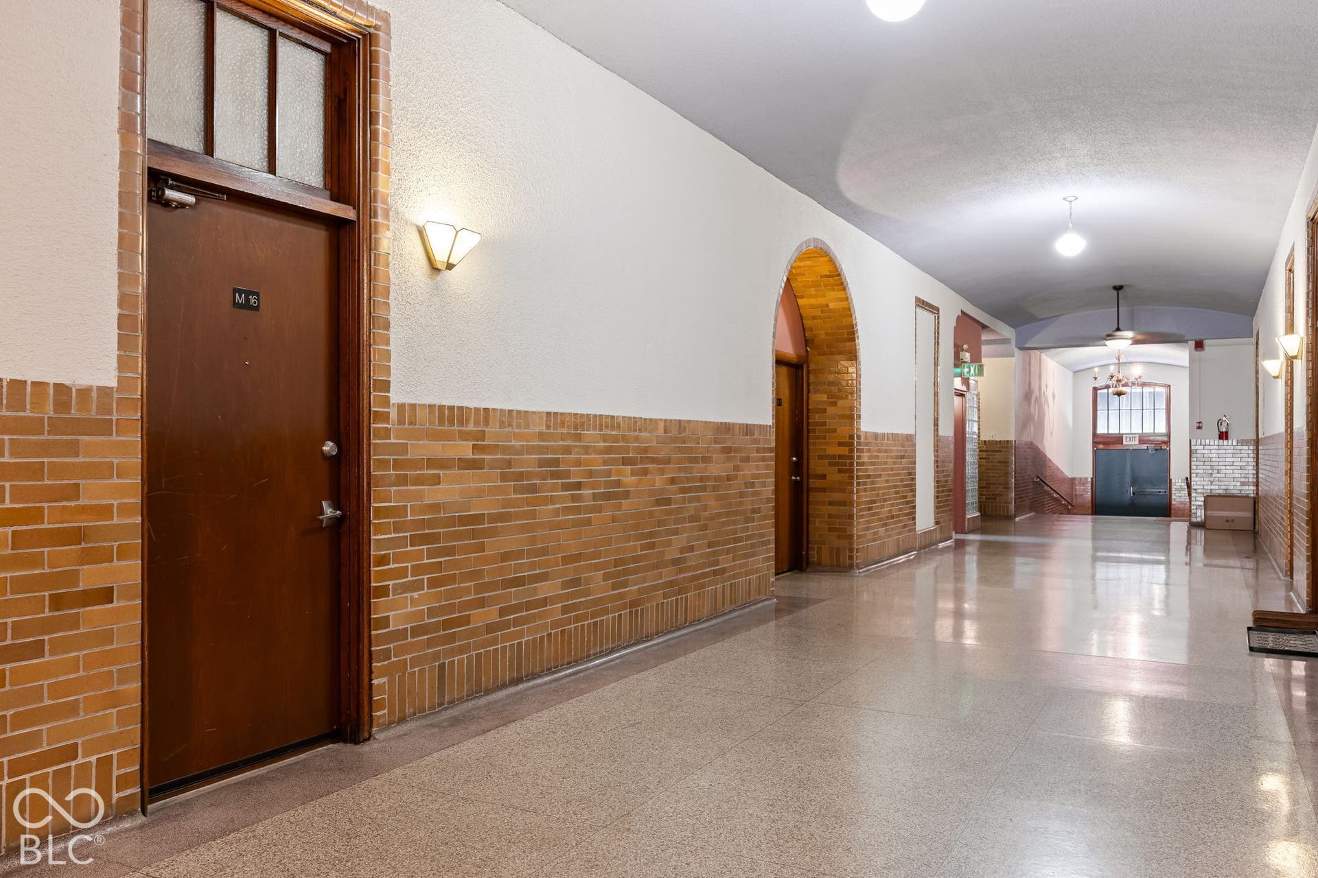 Hallway featuring arched brick entryways, wainscoting with brick detailing, solid wood doors with transom windows, stone-finish flooring, and wall-mounted sconce lighting