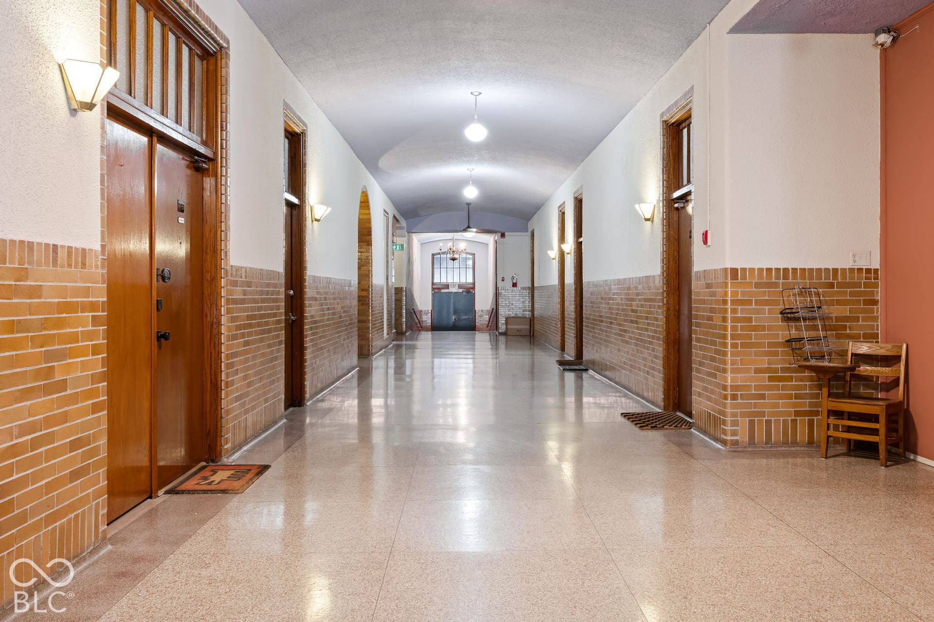 Hallway featuring arched ceilings, polished stone flooring, brick wainscoting, and wood-trim door frames with transom windows