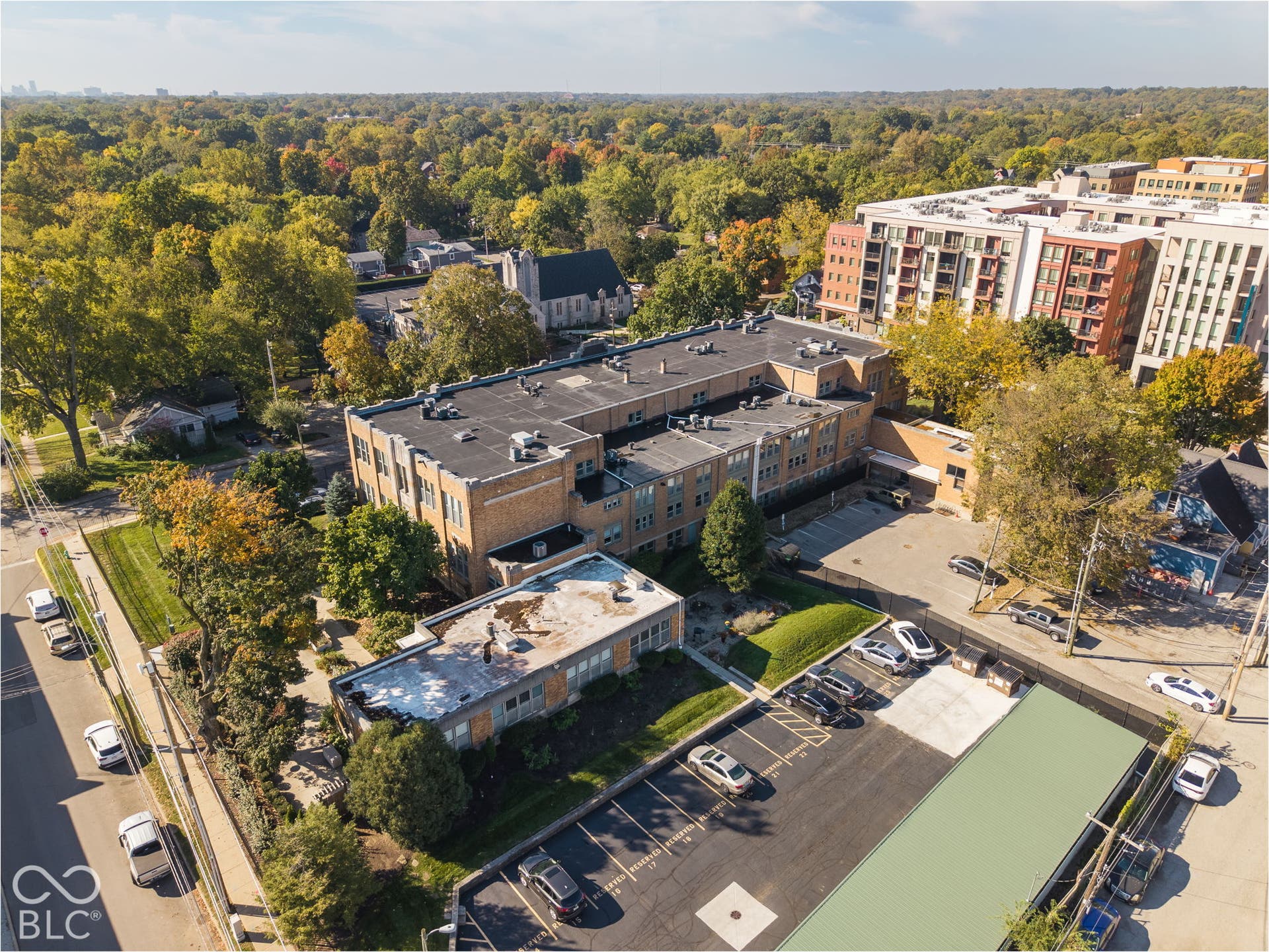 Aerial perspective of a multi-story masonry building with a dedicated paved parking lot, flat roofing, and established perimeter landscaping