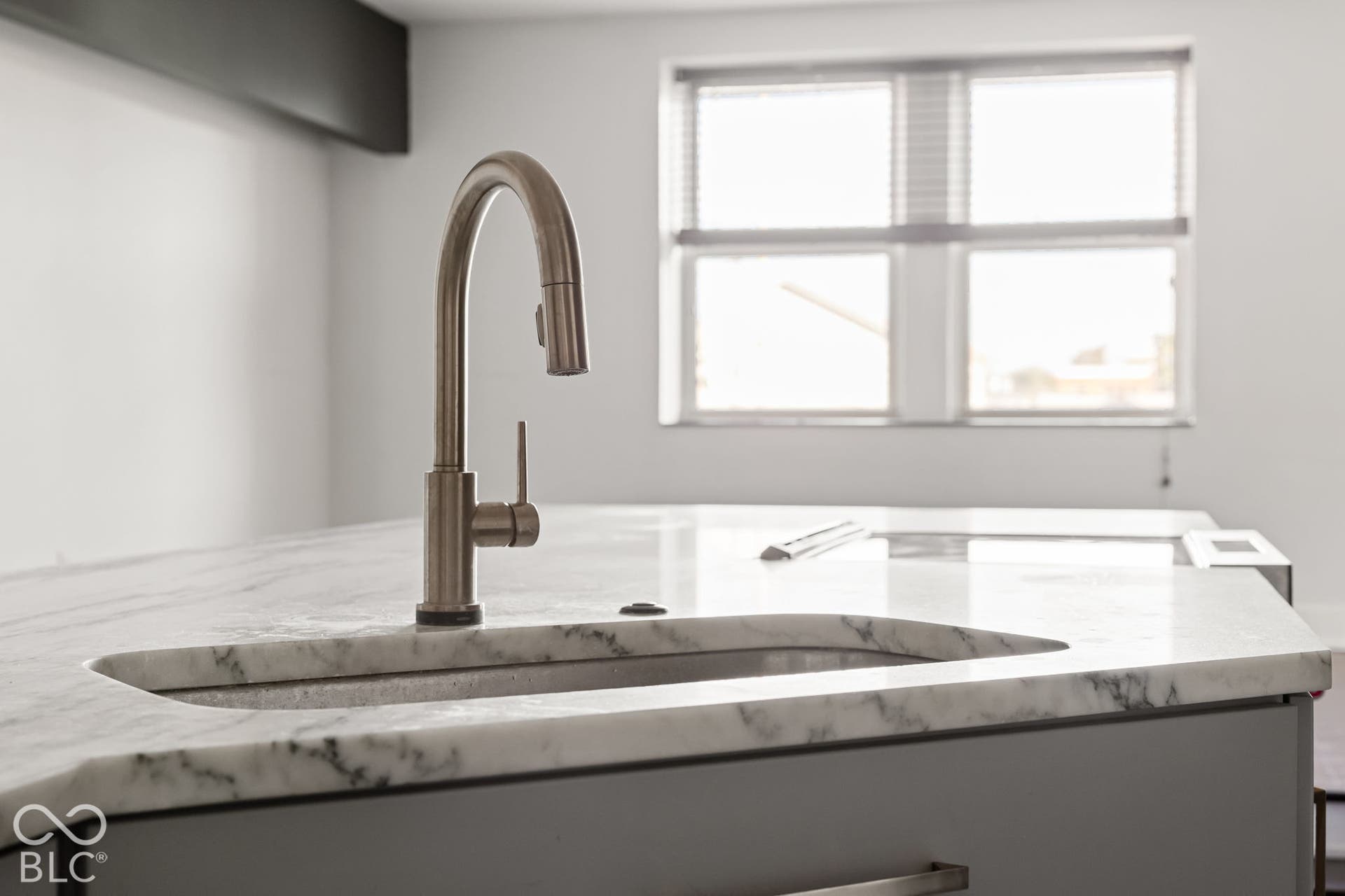 Kitchen island featuring a stone-surface countertop, an integrated undermount sink, and a brushed-finish high-arc pull-down faucet