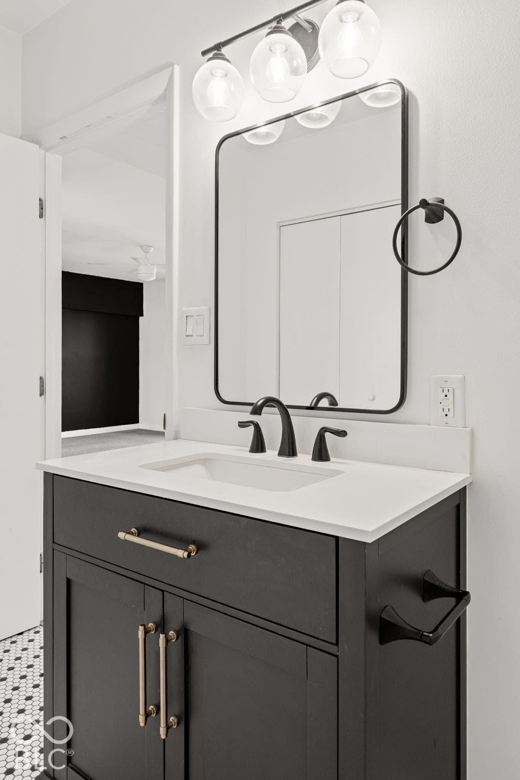 Dark-toned vanity with brass hardware, solid surface countertop, rectangular under-mount sink, black-framed mirror, and globe-style vanity lighting
