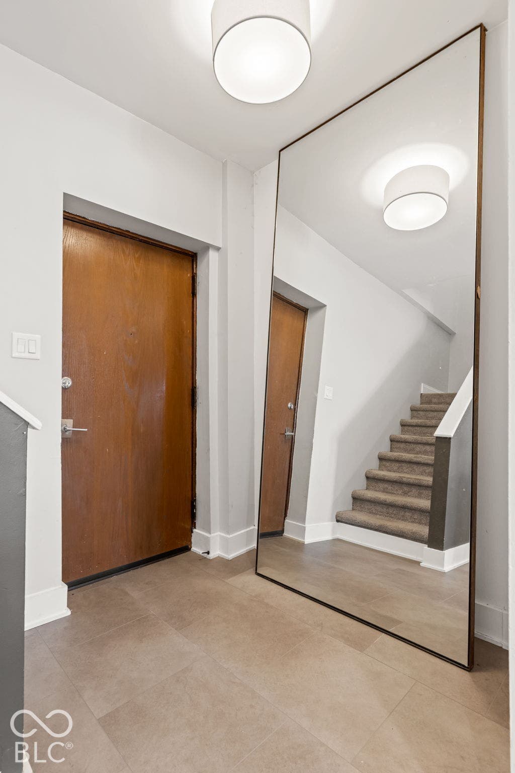 Entryway featuring large-format tile flooring, a floor-to-ceiling mirror with a thin metallic frame, a flush-mount drum light fixture, and a solid wood entry door